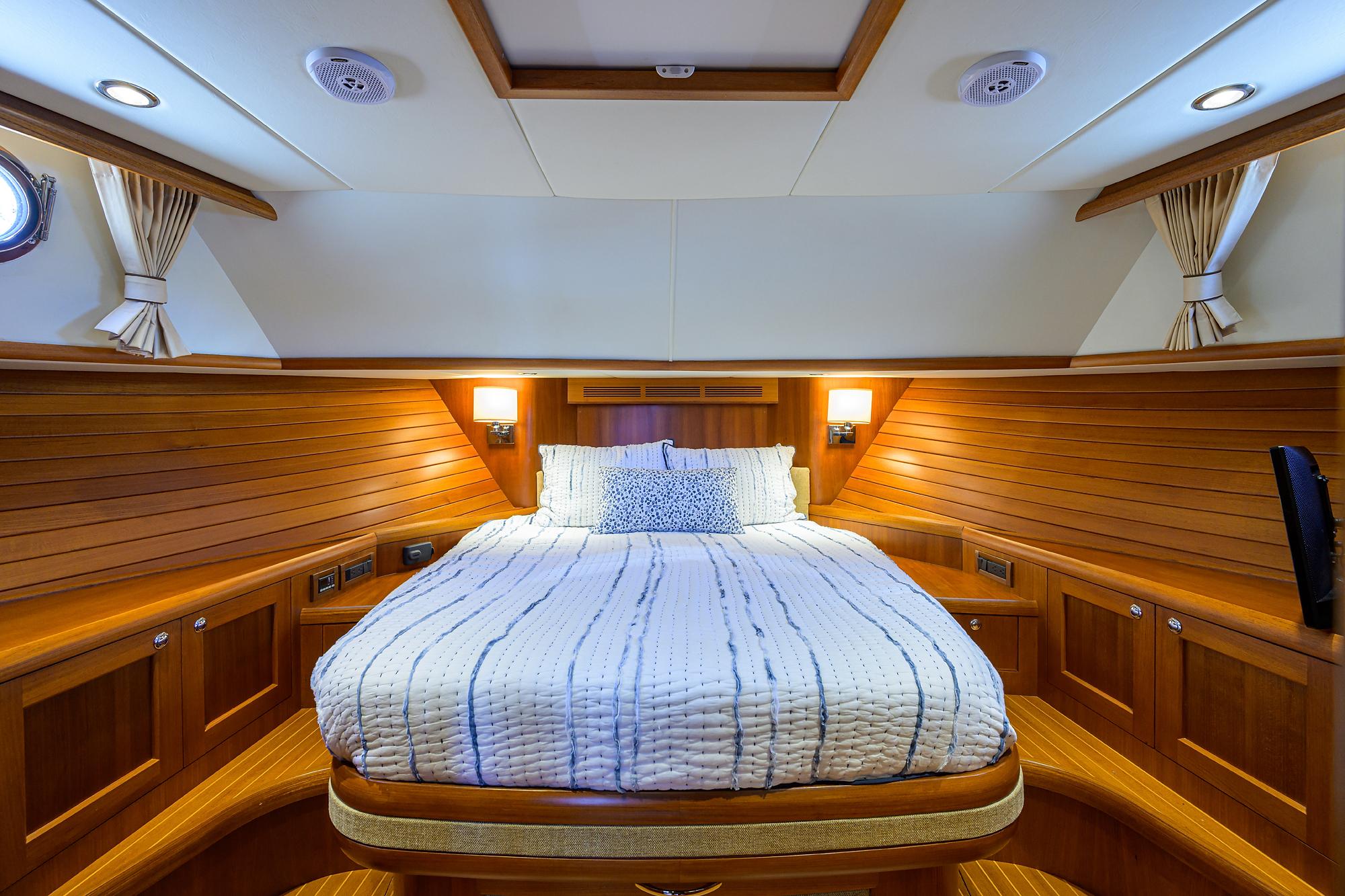 Luxurious cabin interior of 2014 Grand Banks 46 Eastbay SX yacht with wood paneling and cozy bed.