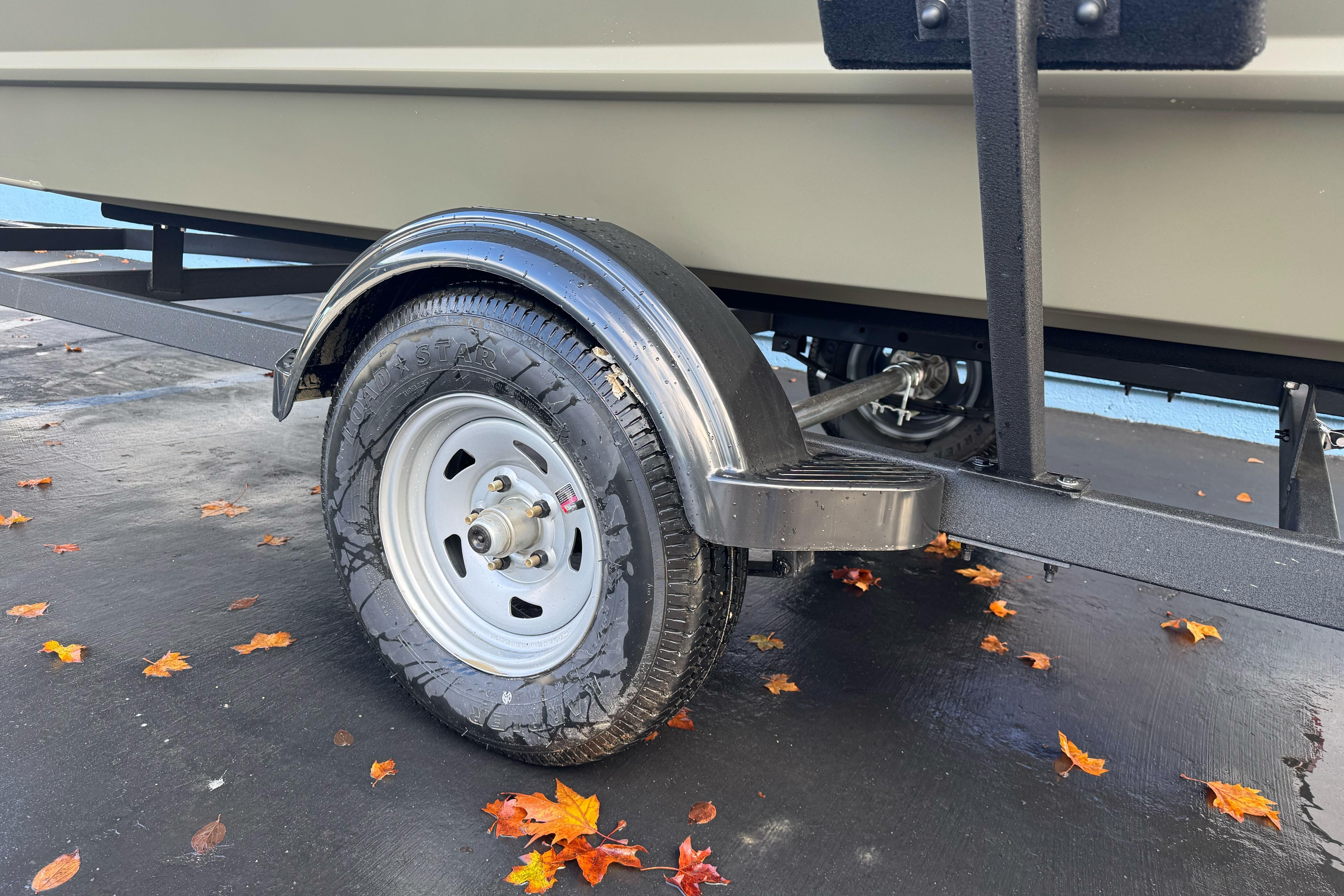 Trailer wheel of 2026 Tracker Grizzly 1654 T Sportsman, surrounded by autumn leaves.