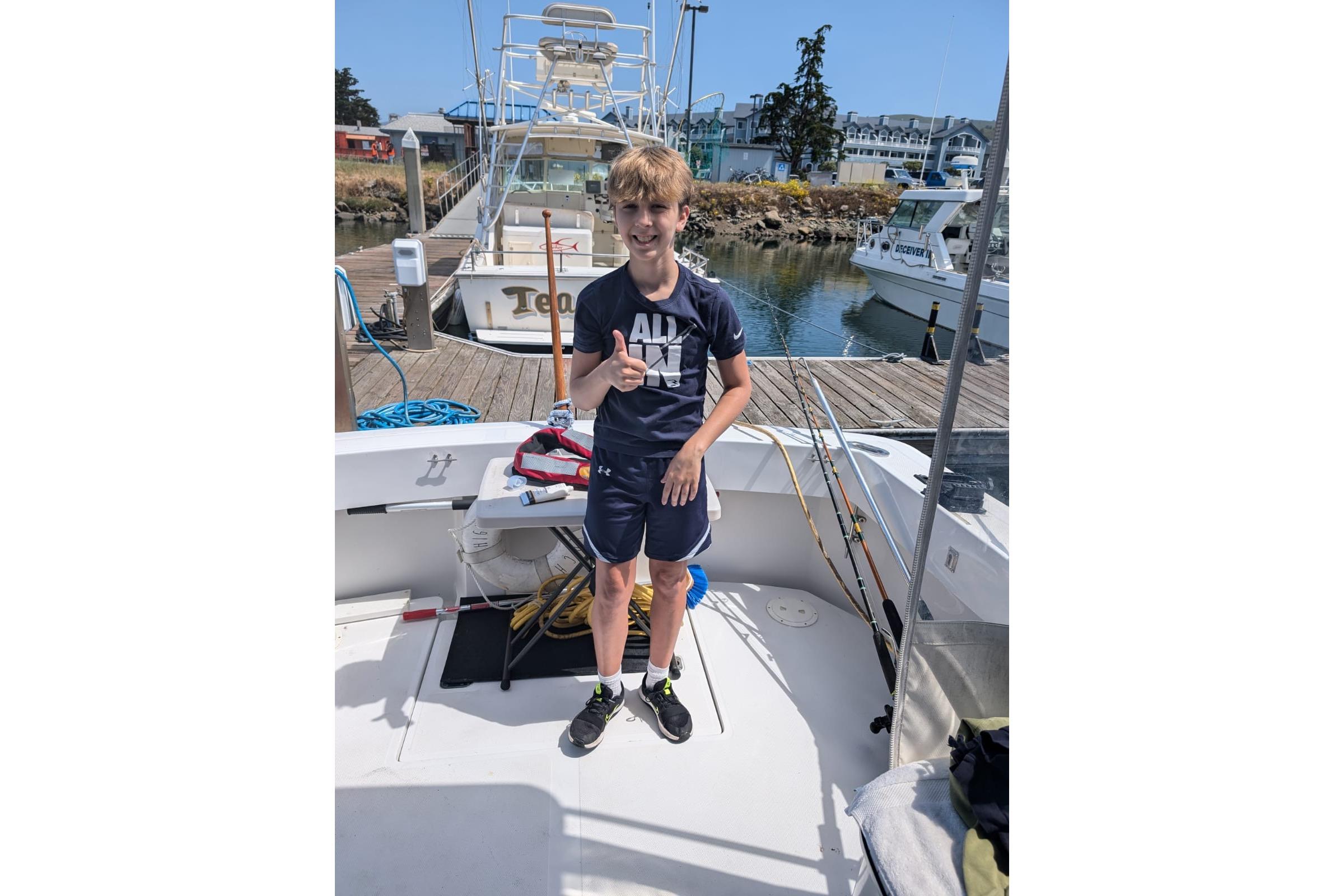 Boy on 1999 Mainship Pilot 30 boat, smiling and giving thumbs up at marina.