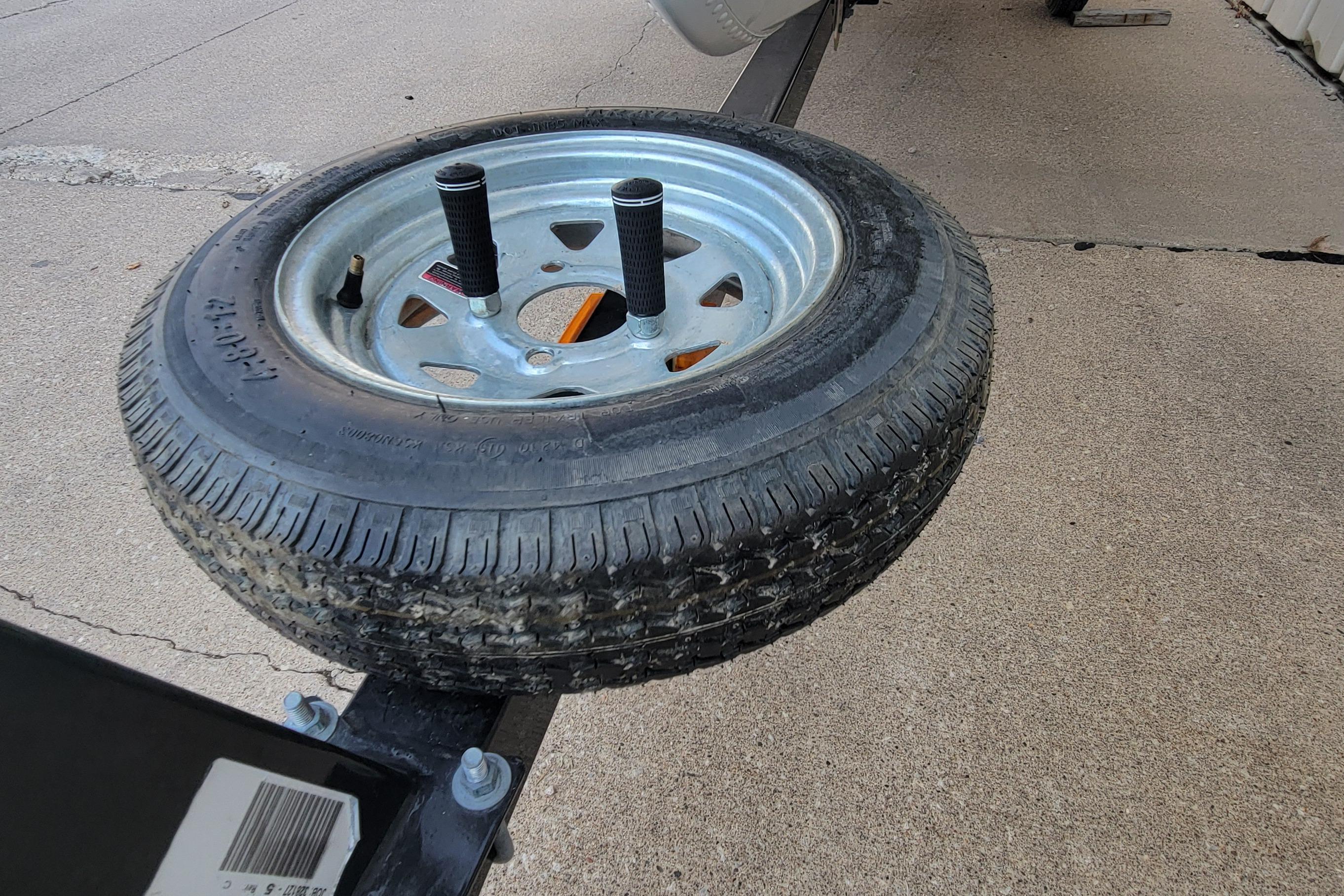 Spare tire mounted on a MirroCraft 1400 trailer, 2014 model, on concrete surface.