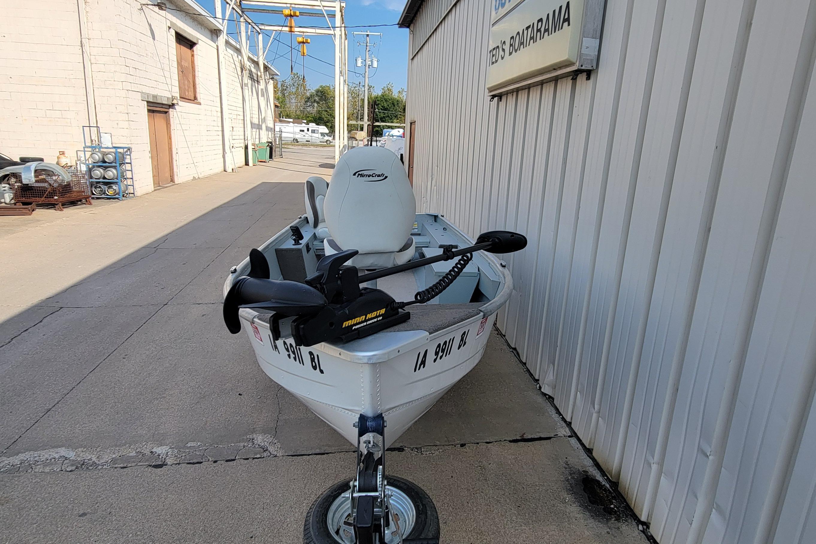 2014 MirroCraft 1400 boat on trailer, parked beside a building.