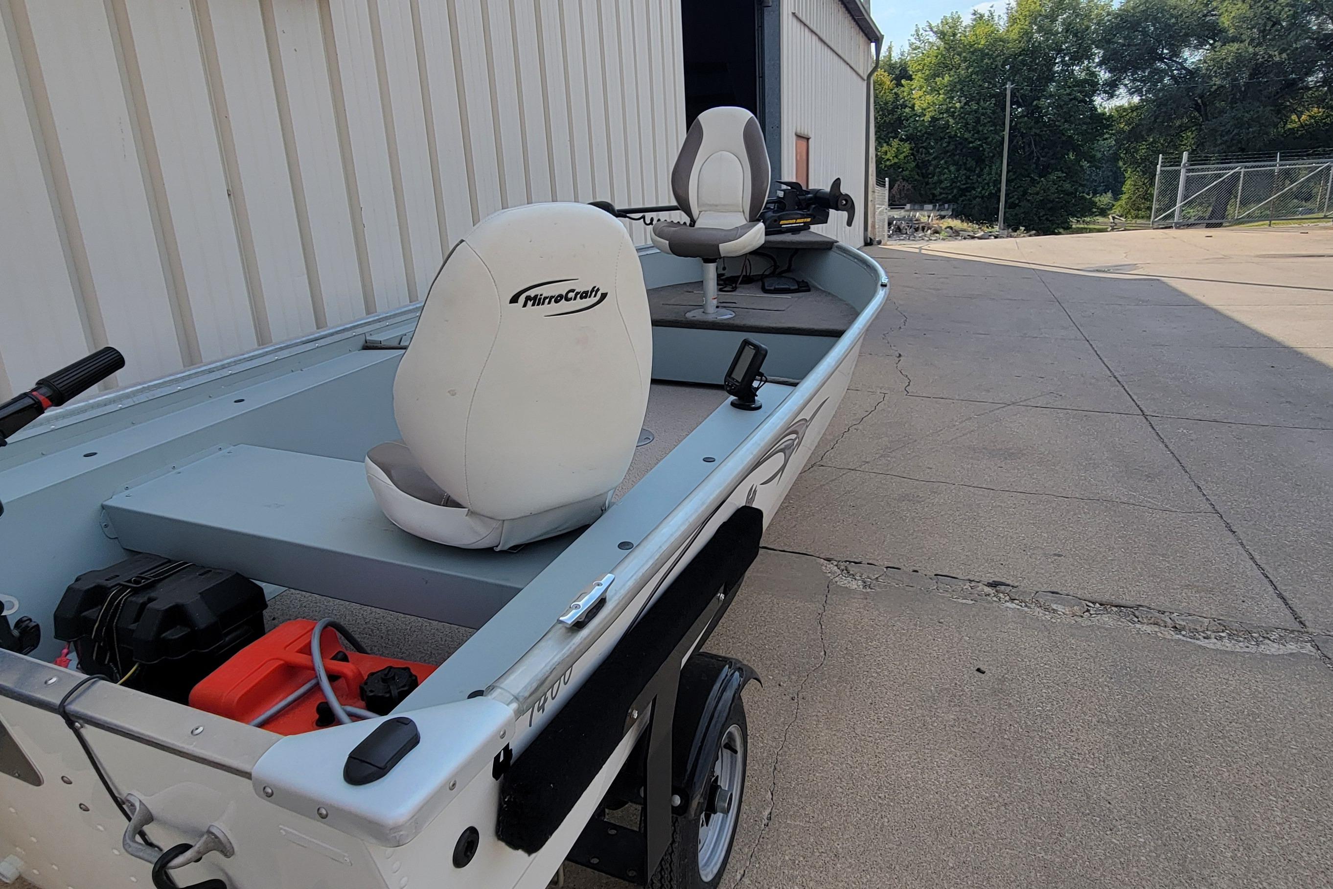 2014 MirroCraft 1400 boat with white seats, parked outside a building.