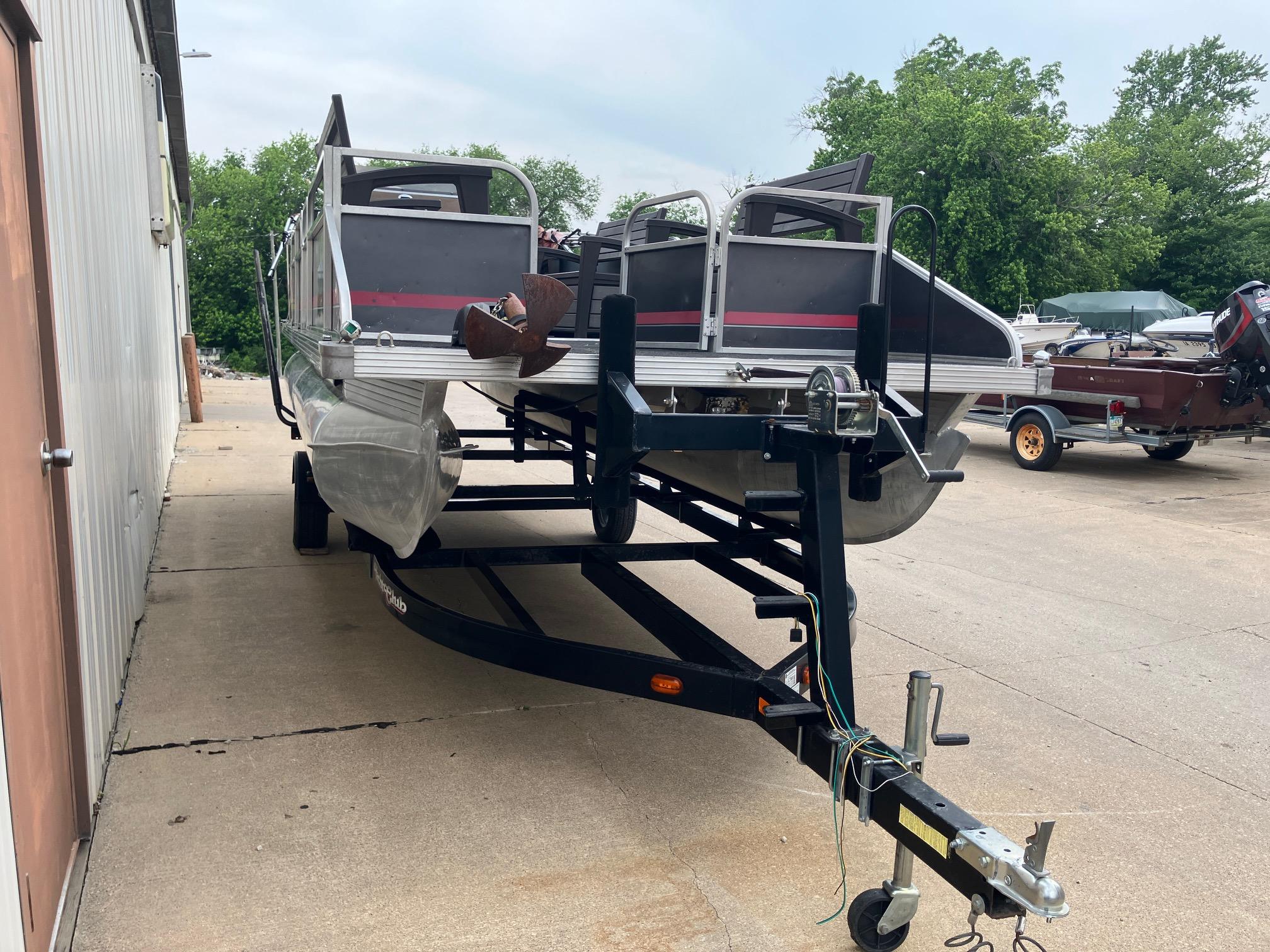 1990 Astro 24' Pontoon boat on trailer, parked outdoors near a building.