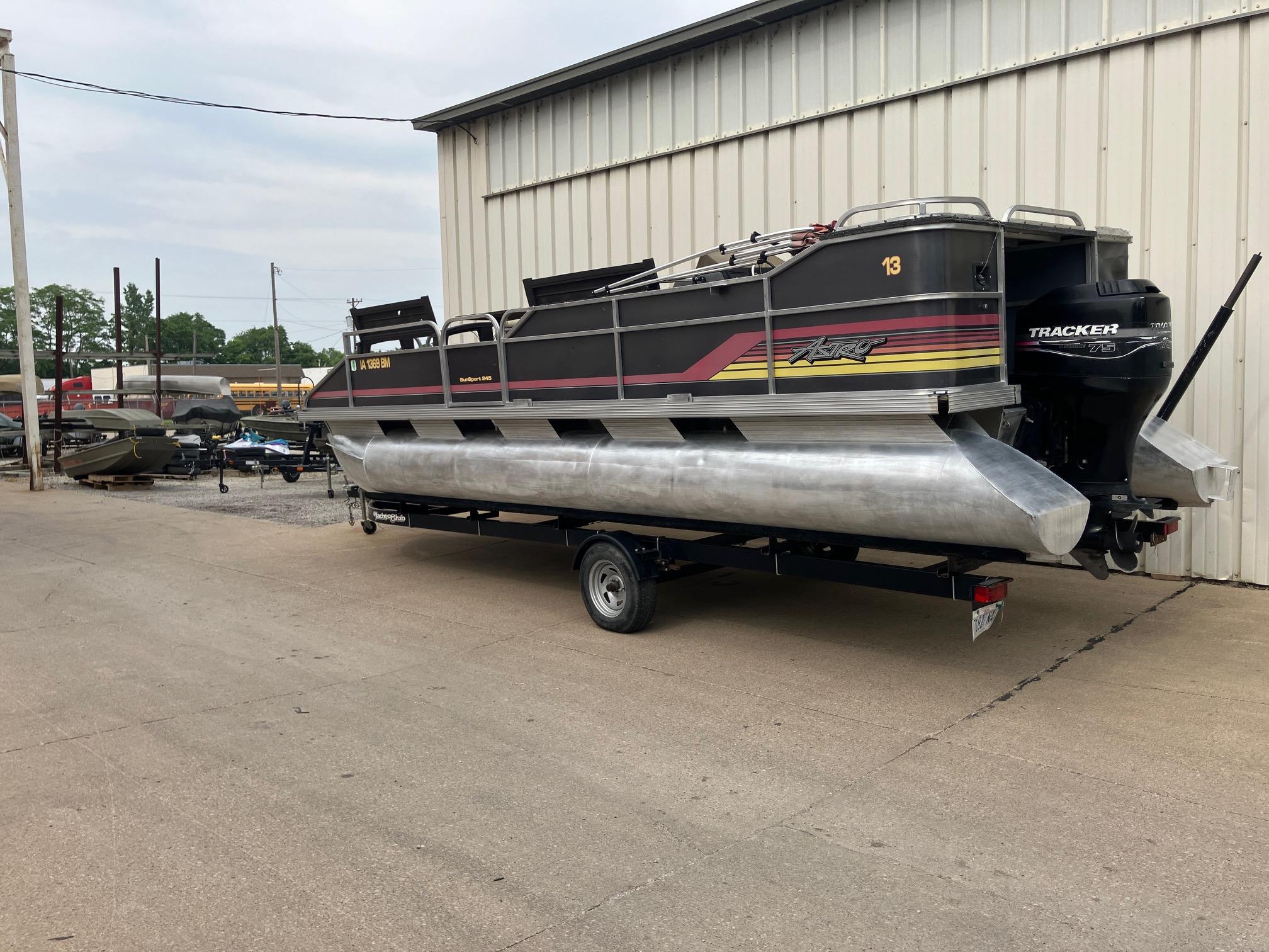 1990 Astro 24' Pontoon boat on trailer, parked outside a warehouse.