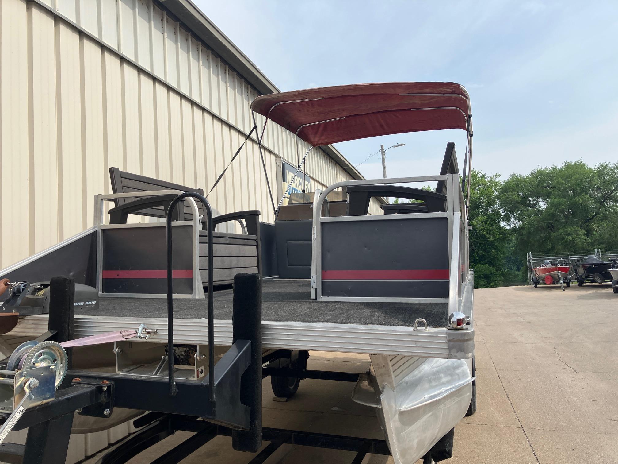 1990 Astro 24' Pontoon boat with red canopy on trailer, parked near a building.