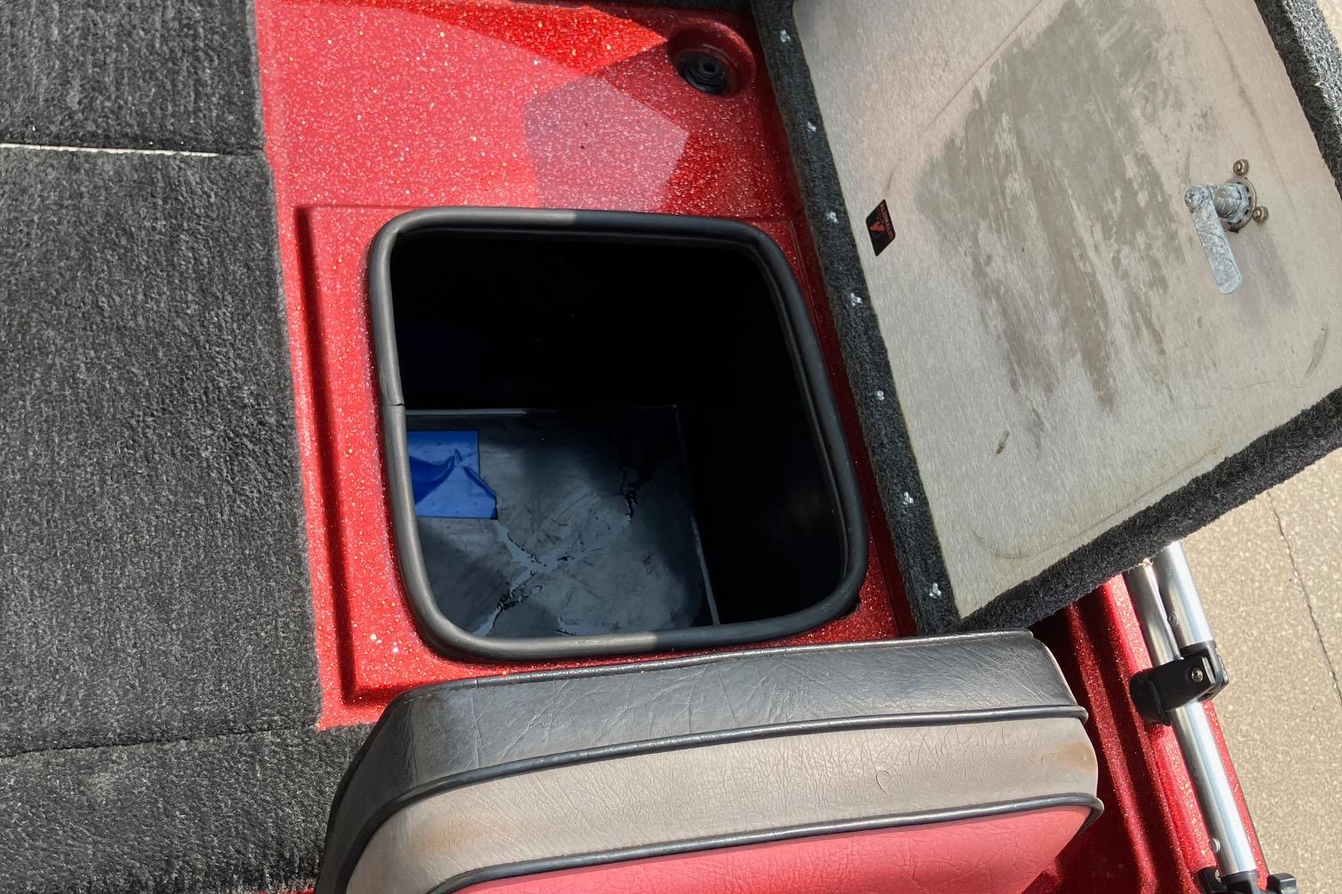 Open storage compartment in 1990 Astro 17 1/2' Bass Boat with red and black interior.
