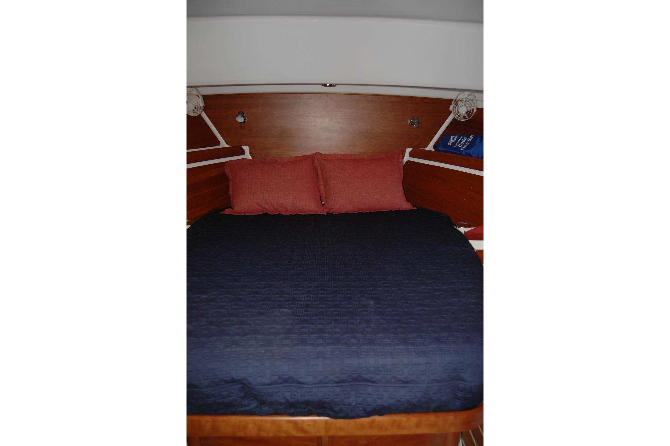 Cozy cabin bed in 2014 Back Cove 34 yacht with navy bedding and red pillows.