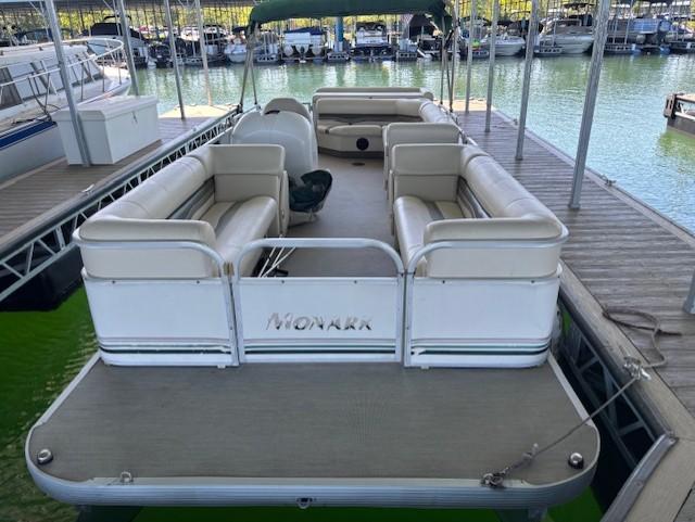 Pontoon boat docked, Monarch 240 model, 2001, with spacious seating and green water backdrop.