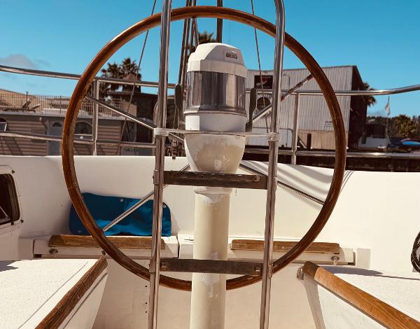 1978 Islander Sloop 36 sailboat cockpit with wooden steering wheel and clear blue sky.
