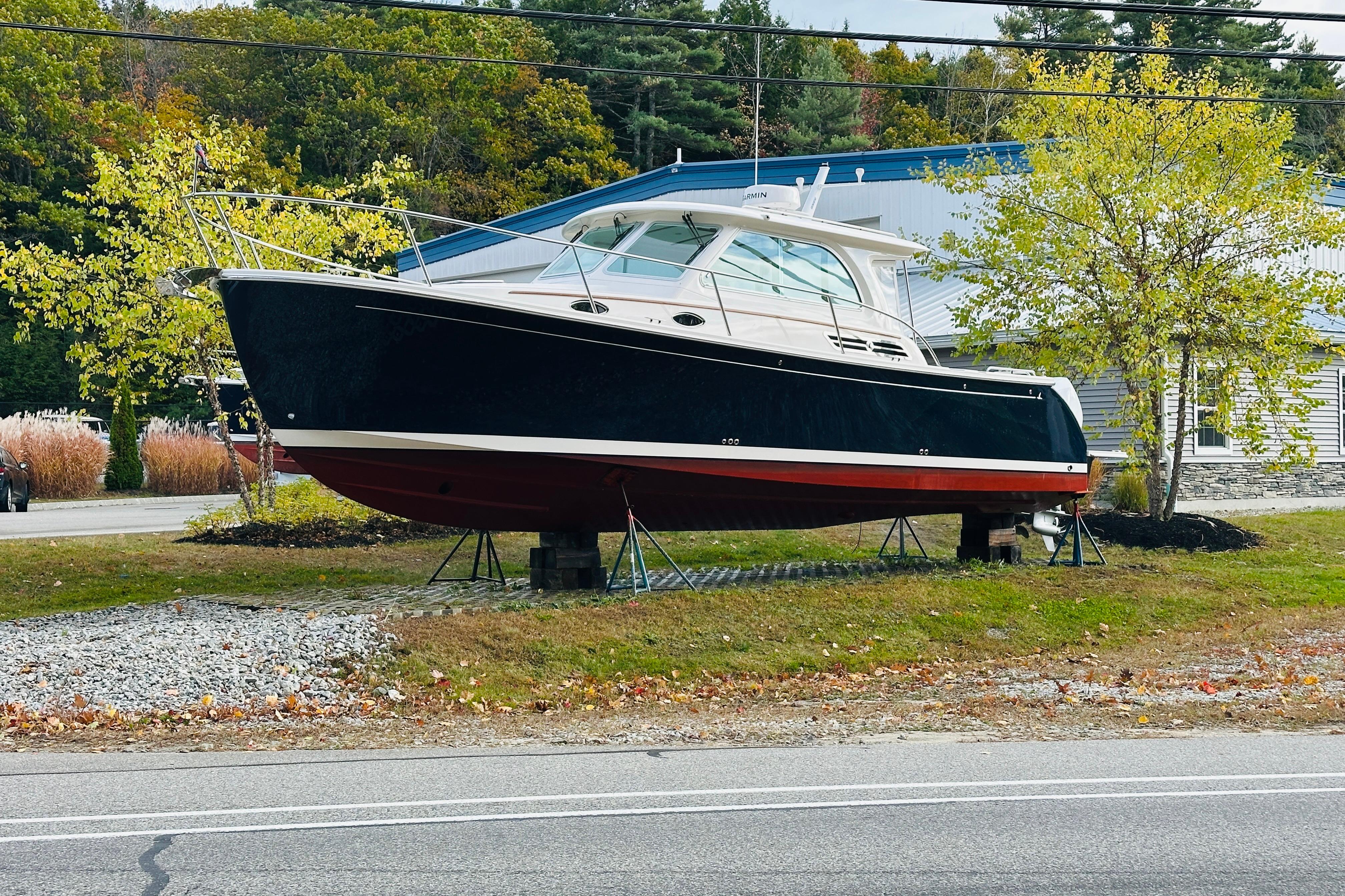 2024 Back Cove 34O boat displayed outdoors on stands, surrounded by trees.