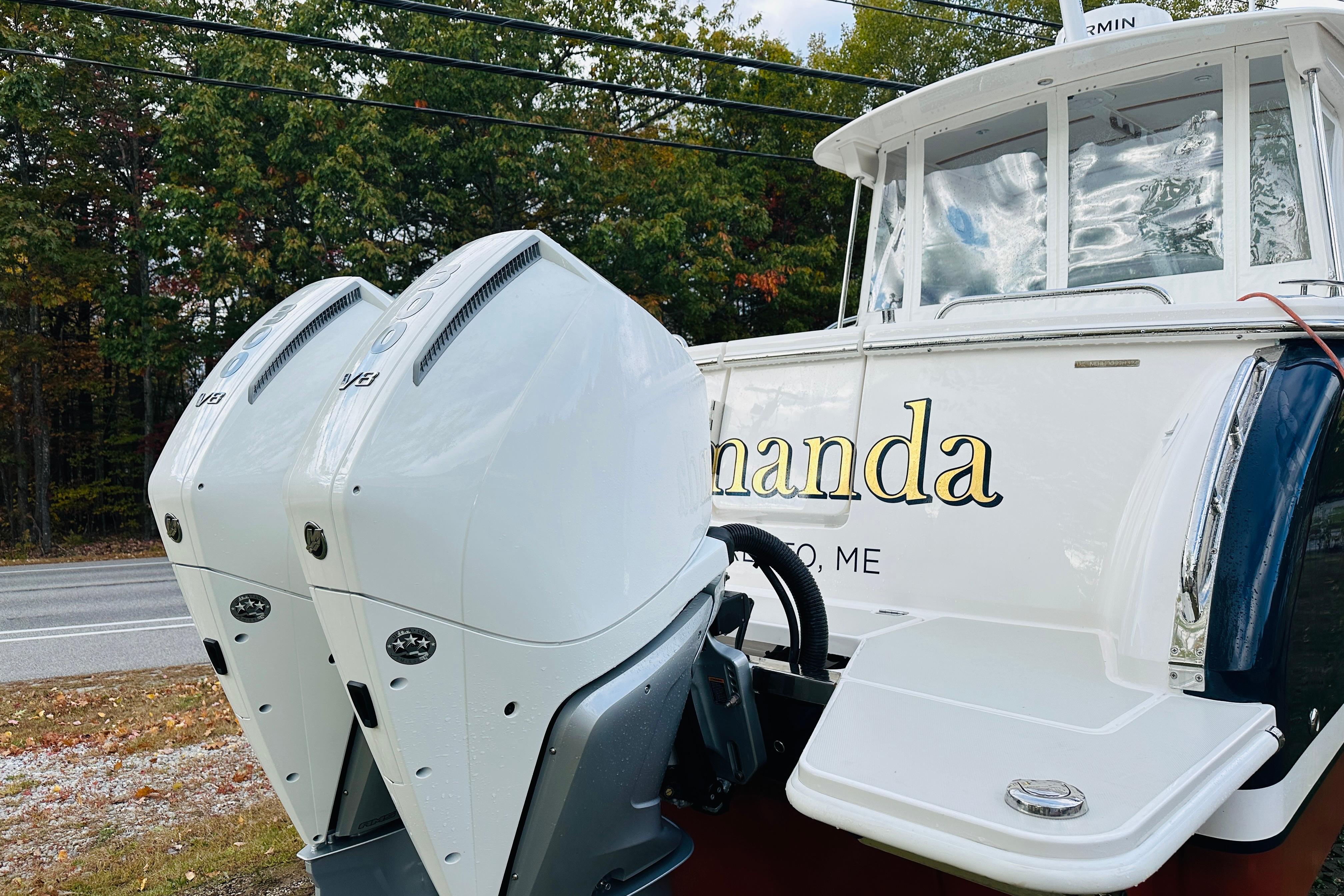 2024 Back Cove 34O boat with dual outboard engines, docked near a wooded area.