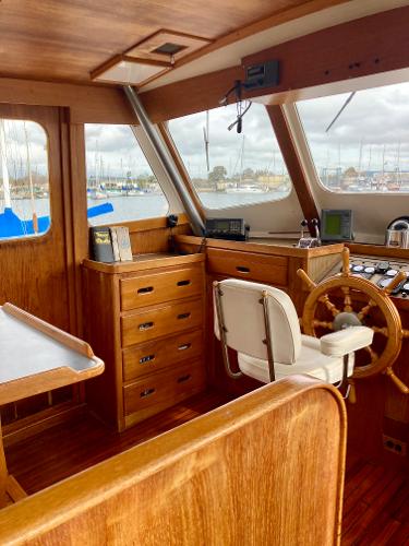 1977 Grand Alaskan Raised Pilothouse interior with wooden helm and marina view.