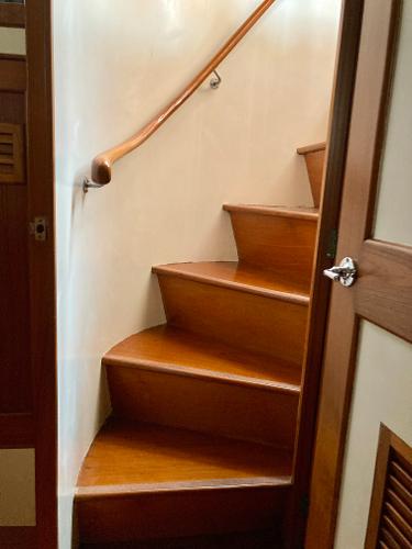 Wooden staircase inside 1977 Grand Alaskan Raised Pilothouse yacht, featuring elegant curved design.