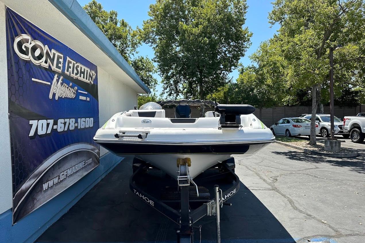 2019 Tahoe 2150 boat on trailer at dealership, surrounded by trees and parked cars.
