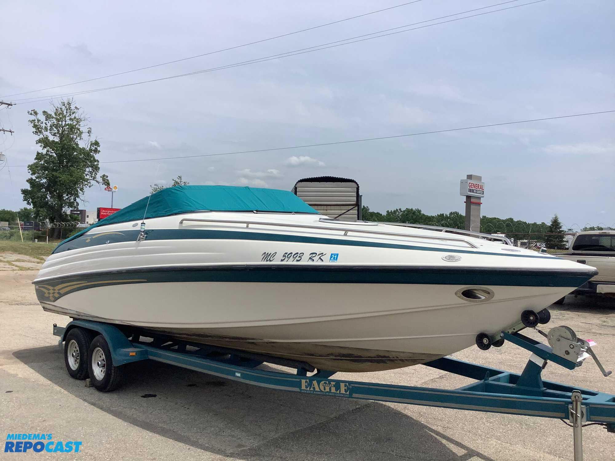 1999 Crownline 266 CCR boat on trailer, parked outdoors, with teal cover.