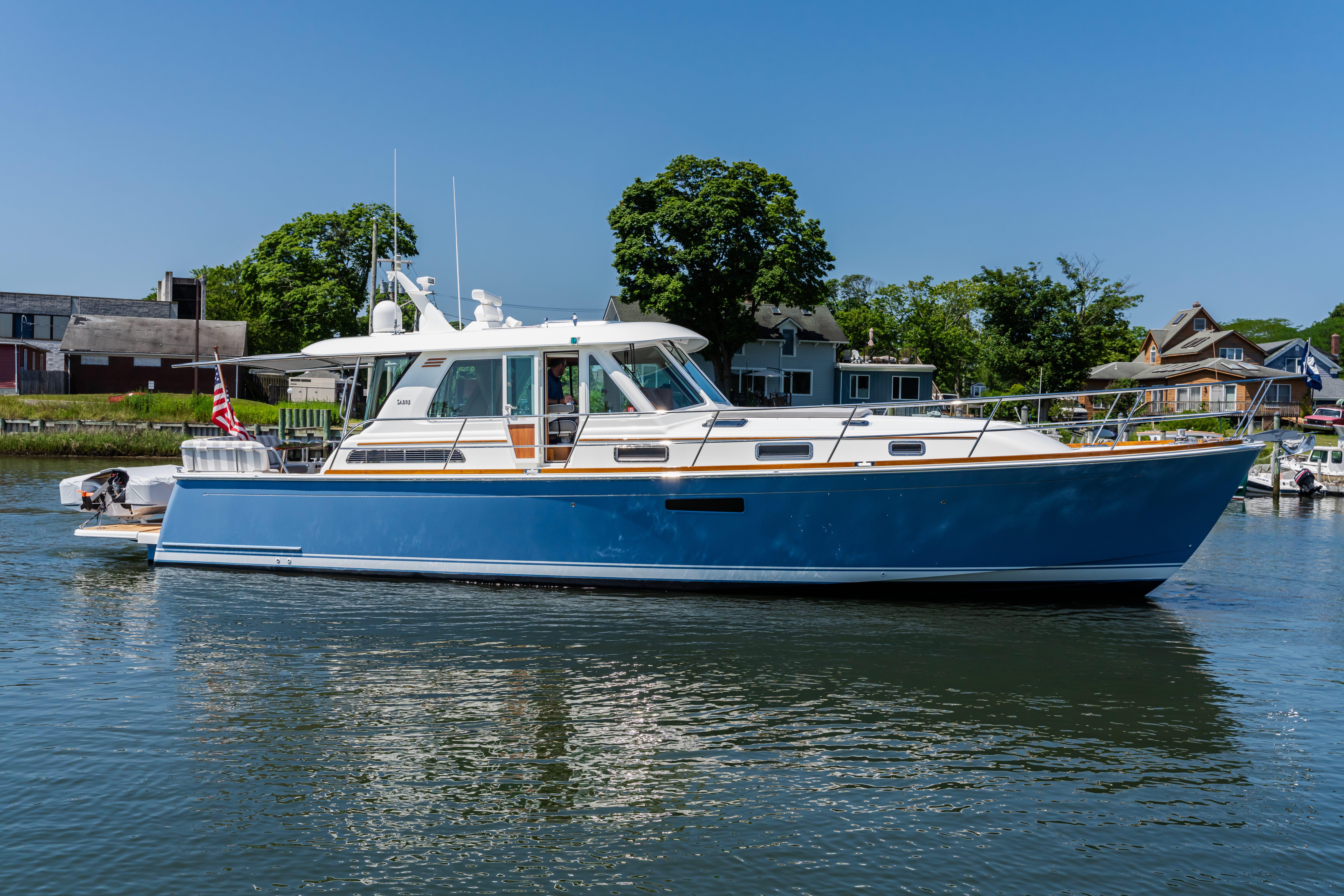 2020 Sabre 48 Salon Express yacht on calm water, with houses and trees in the background.