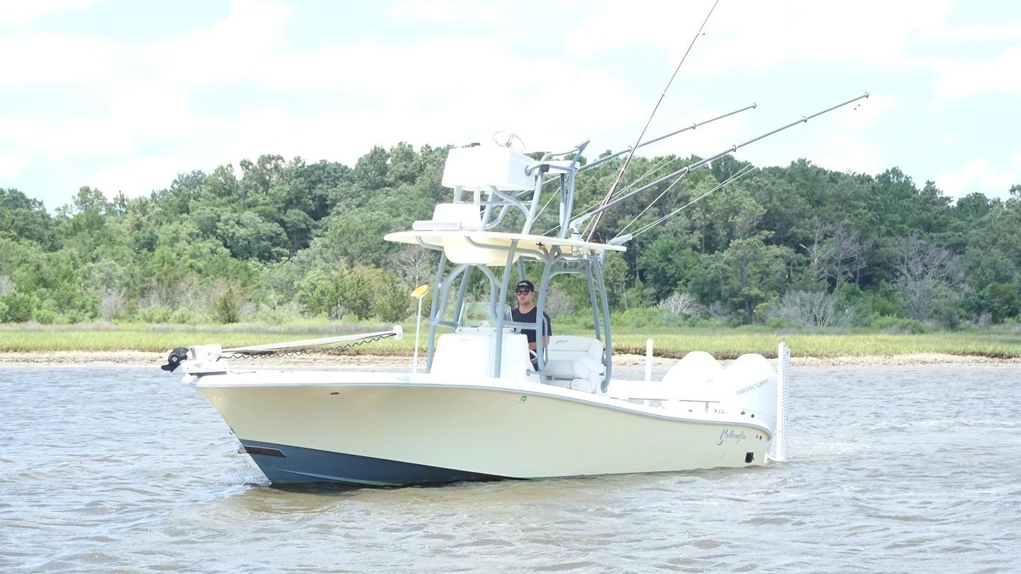 2020 Yellowfin 26 Hybrid boat on water with fishing rods, surrounded by lush greenery.