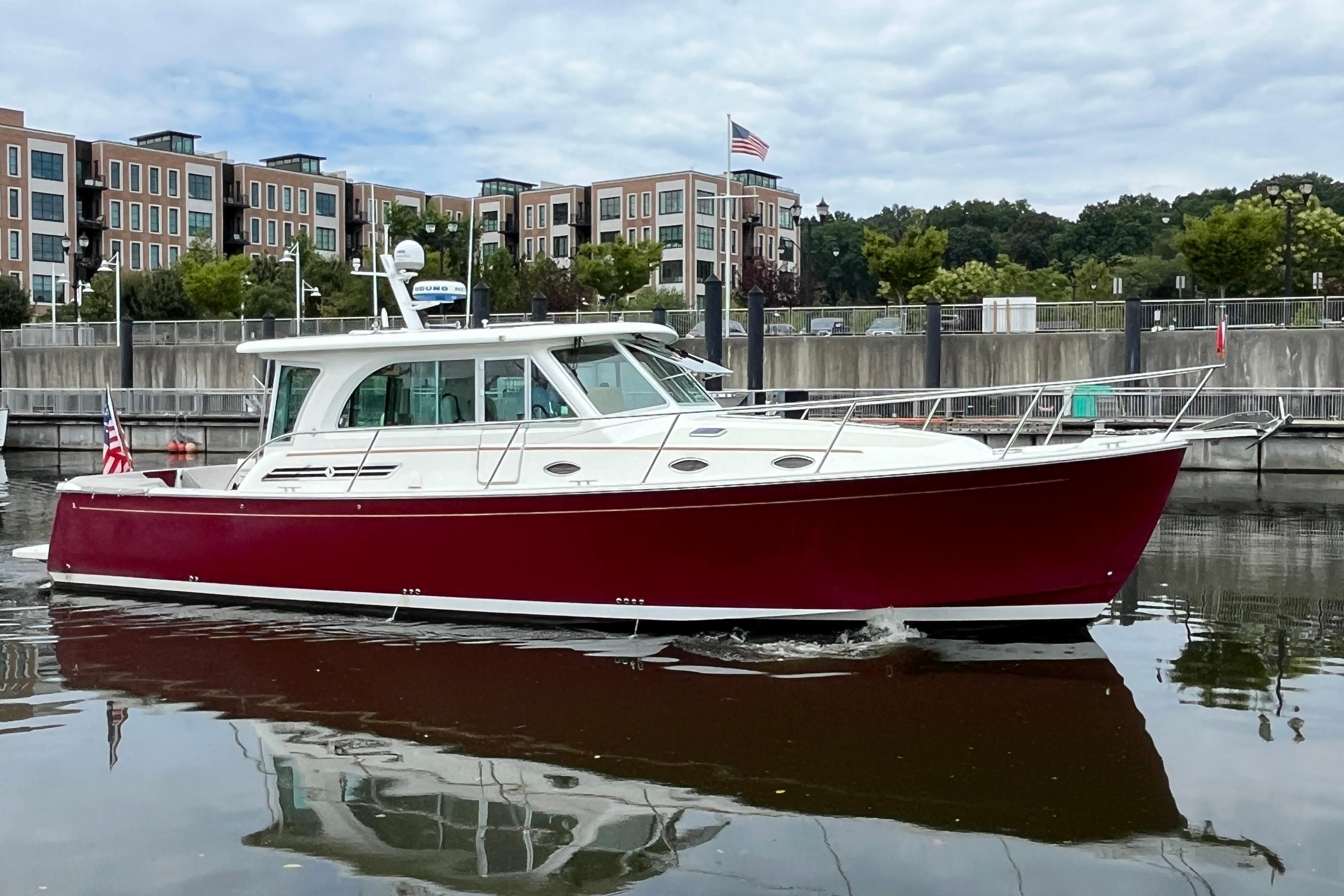 2017 Back Cove 41 boat with red hull docked in a marina, modern buildings in background.
