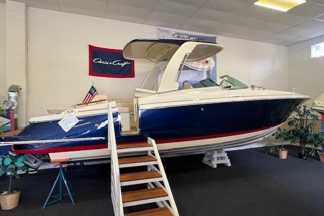 2025 Chris-Craft Launch 28 GT boat displayed indoors with American flag and stairs.