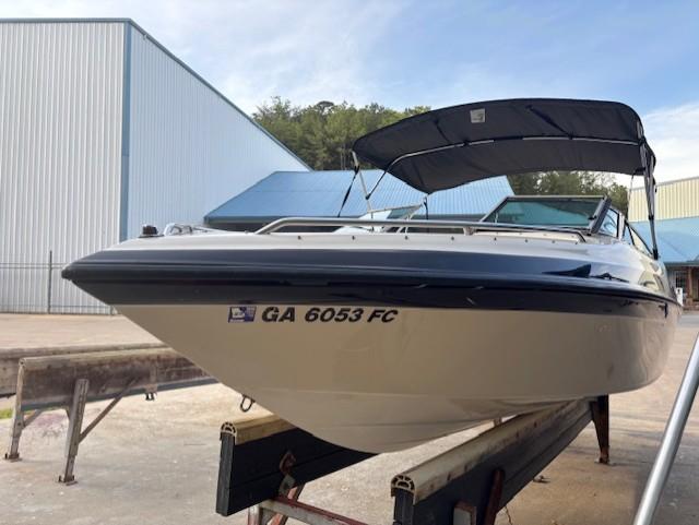 1999 Crownline 202 boat on trailer, with canopy, parked near industrial buildings.