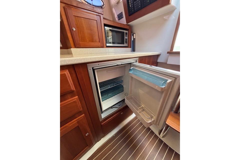 2018 Back Cove 30 yacht kitchen with open fridge, microwave, and wooden cabinetry.