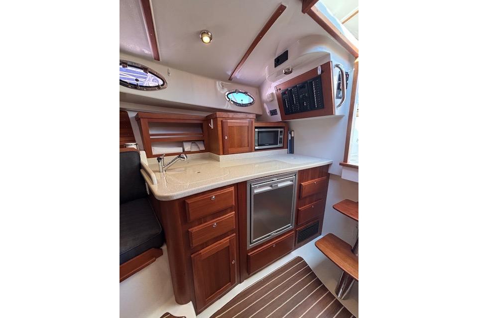 2018 Back Cove 30 yacht interior with kitchenette, featuring wood cabinetry and modern appliances.