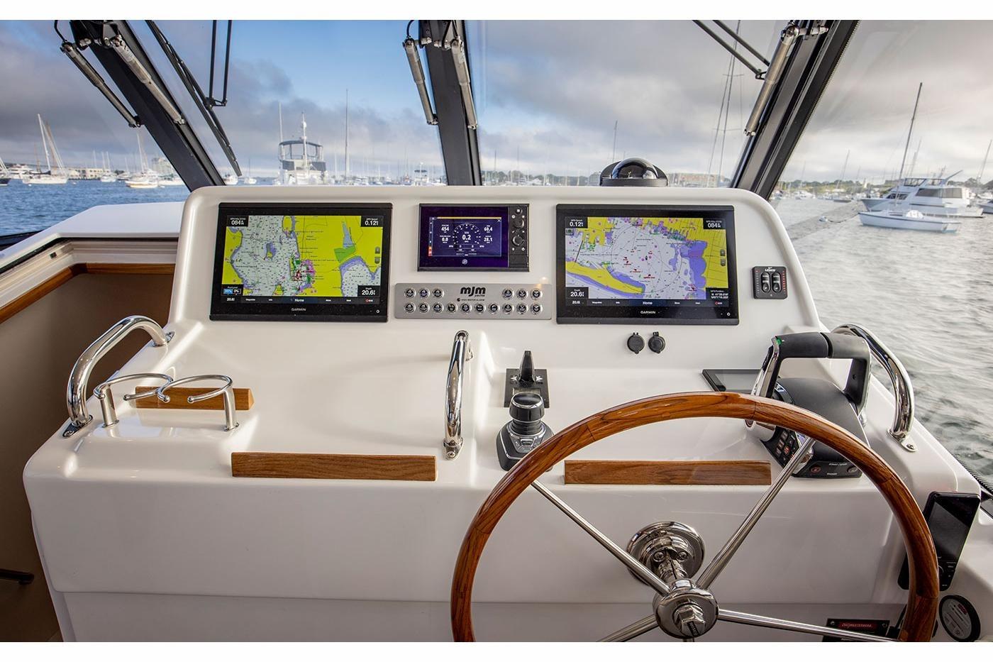 Helm of 2025 MJM 4 boat with navigation screens and wooden steering wheel.