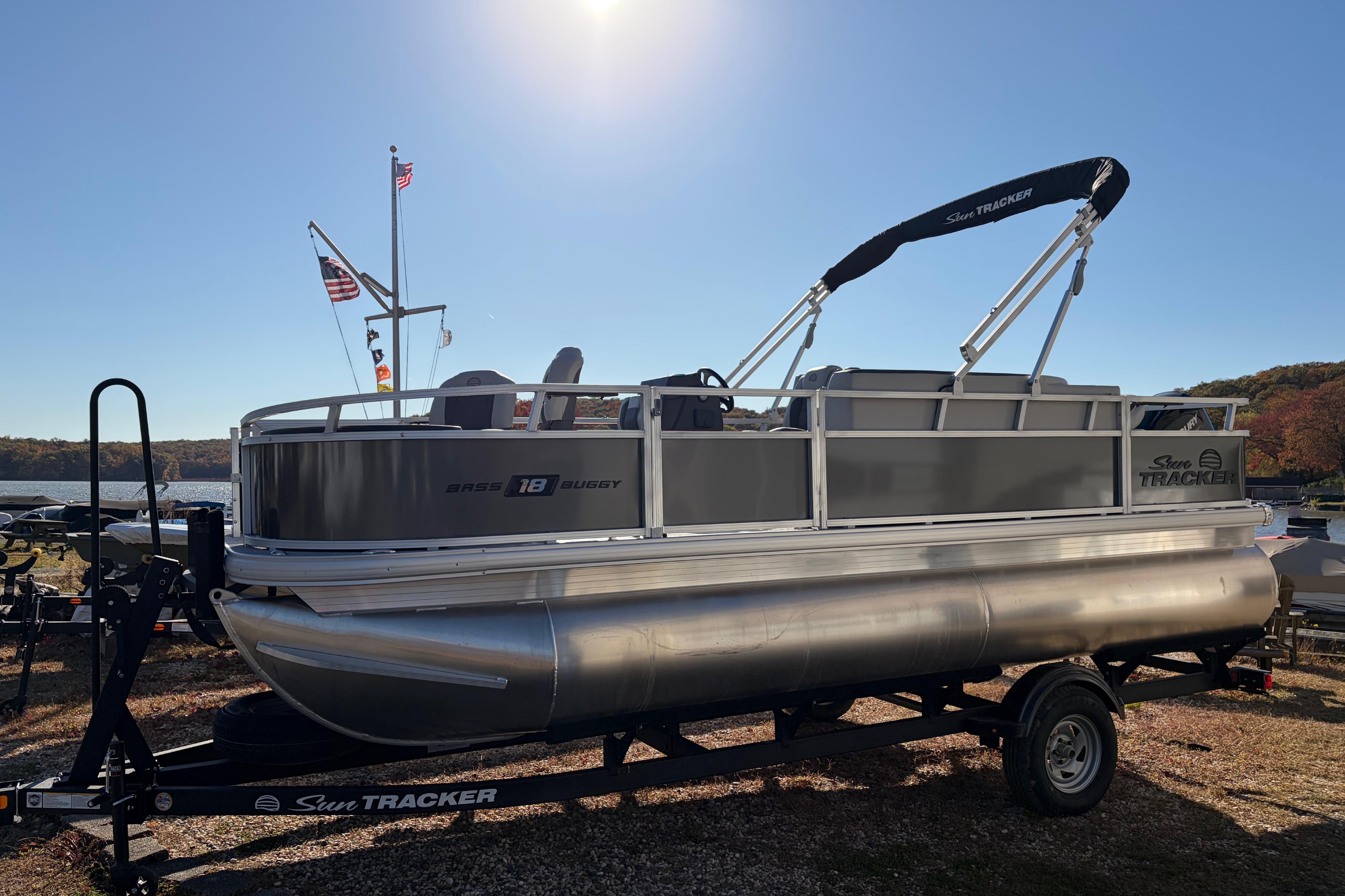 2026 Sun Tracker Bass Buggy 18 DLX pontoon boat on trailer by a lake.