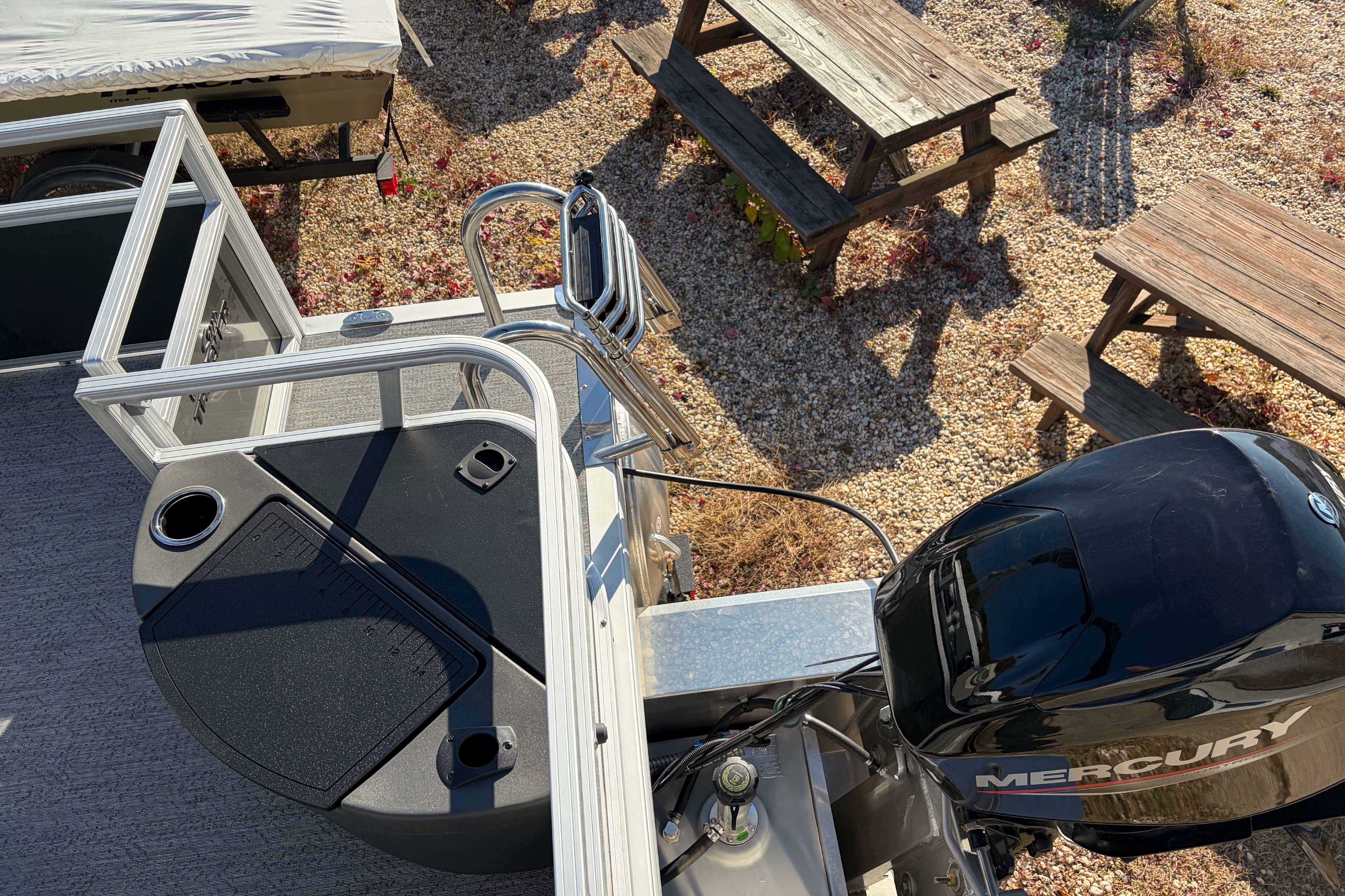 2026 Sun Tracker Bass Buggy 18 DLX pontoon boat with Mercury engine, docked near picnic tables.