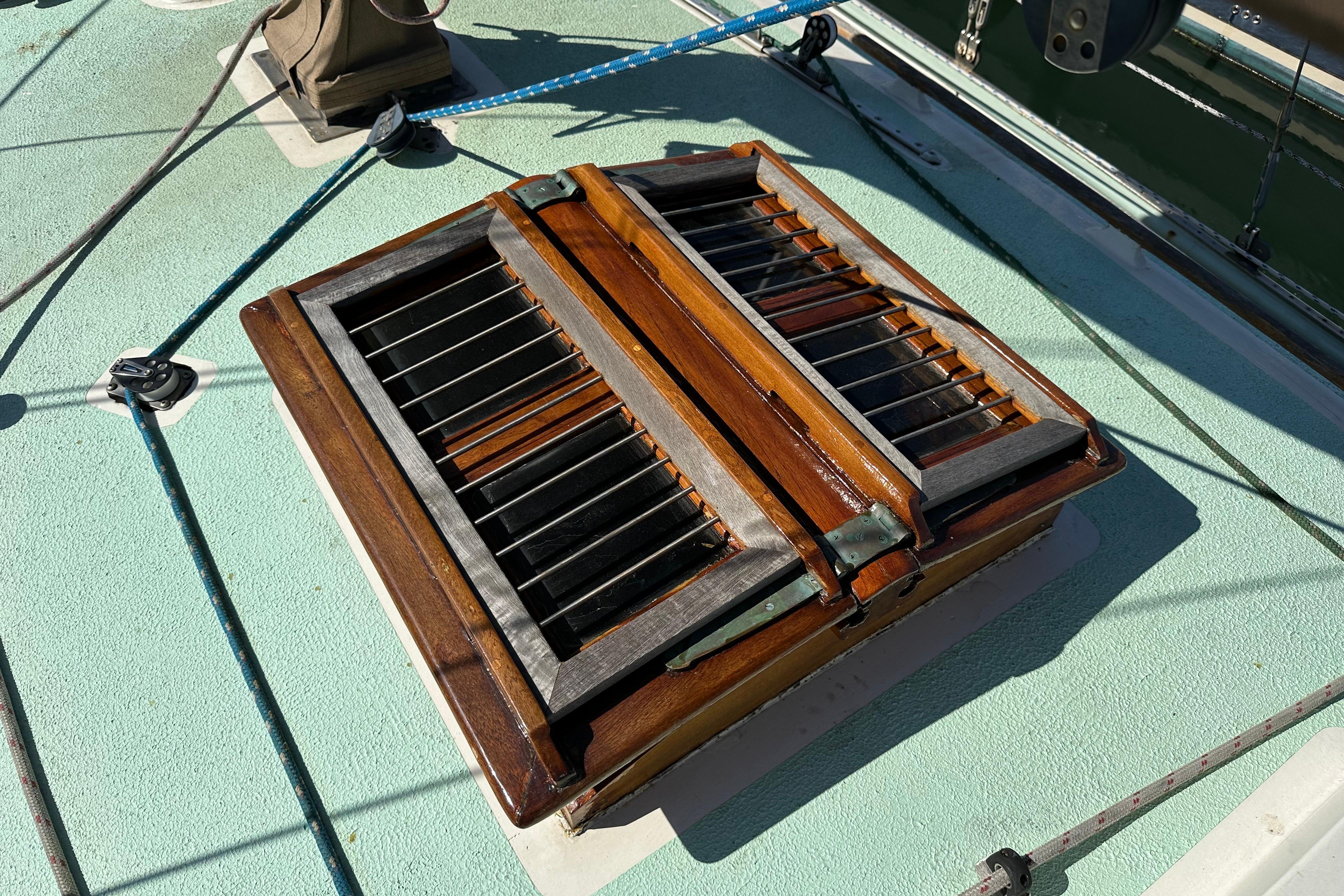 Wooden hatch on 1978 Tayana 37 sailboat deck, featuring metal bars and ropes.