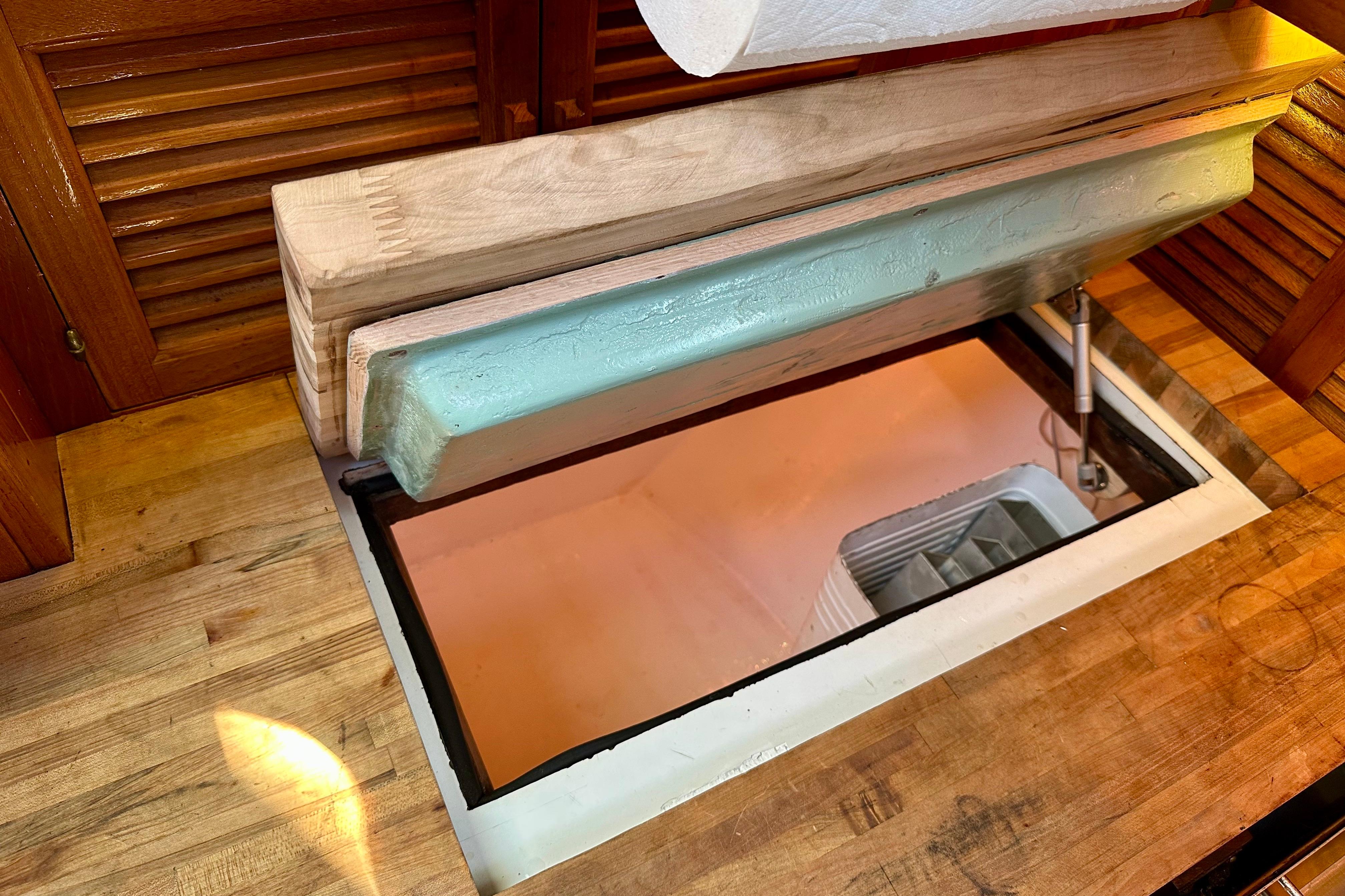 Wooden countertop with open hatch revealing storage in 1978 Tayana 37 sailboat interior.