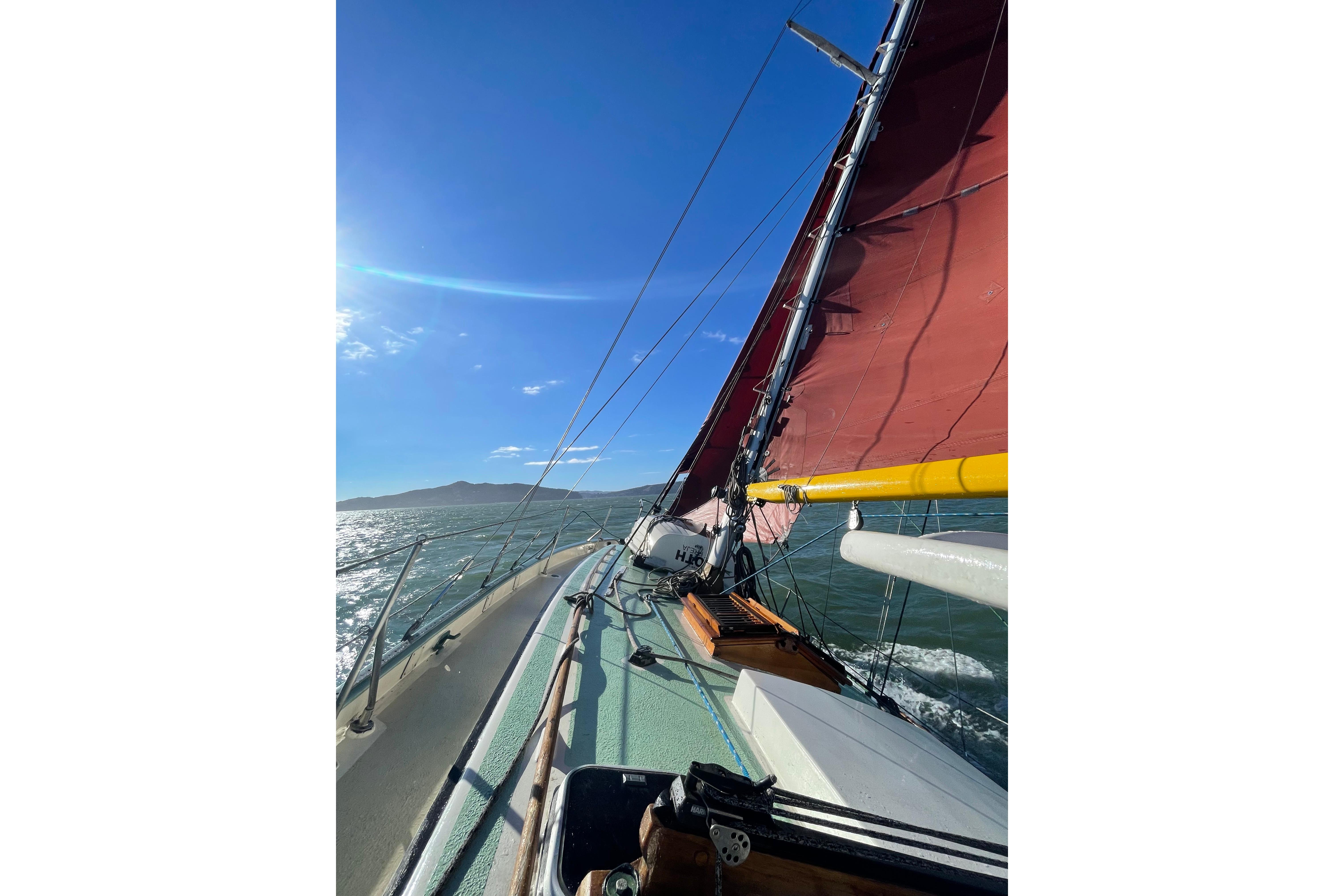 1978 Tayana 37 sailboat with red sails on open water under clear blue sky.