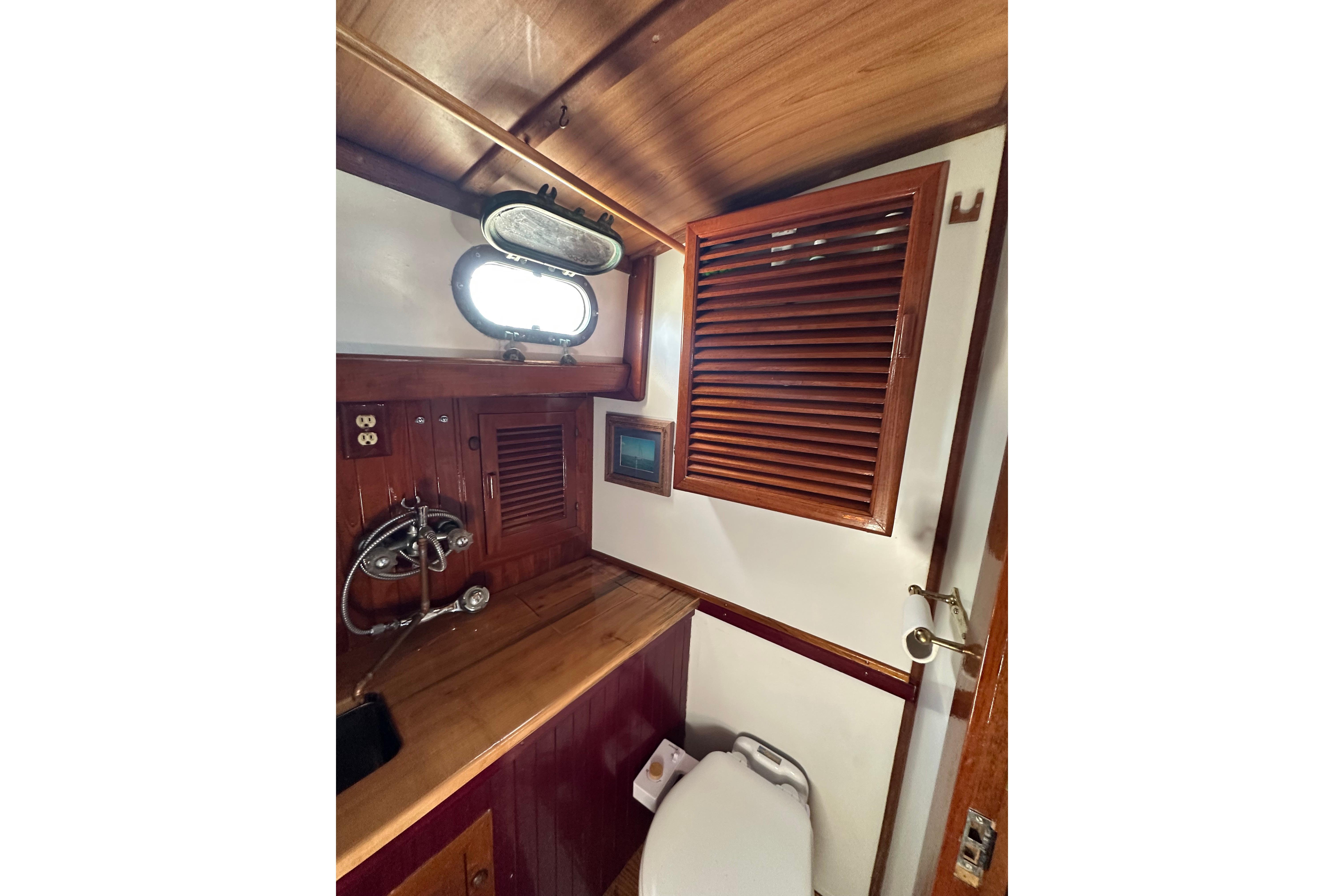 1978 Tayana 37 yacht bathroom with wooden cabinetry and porthole window.