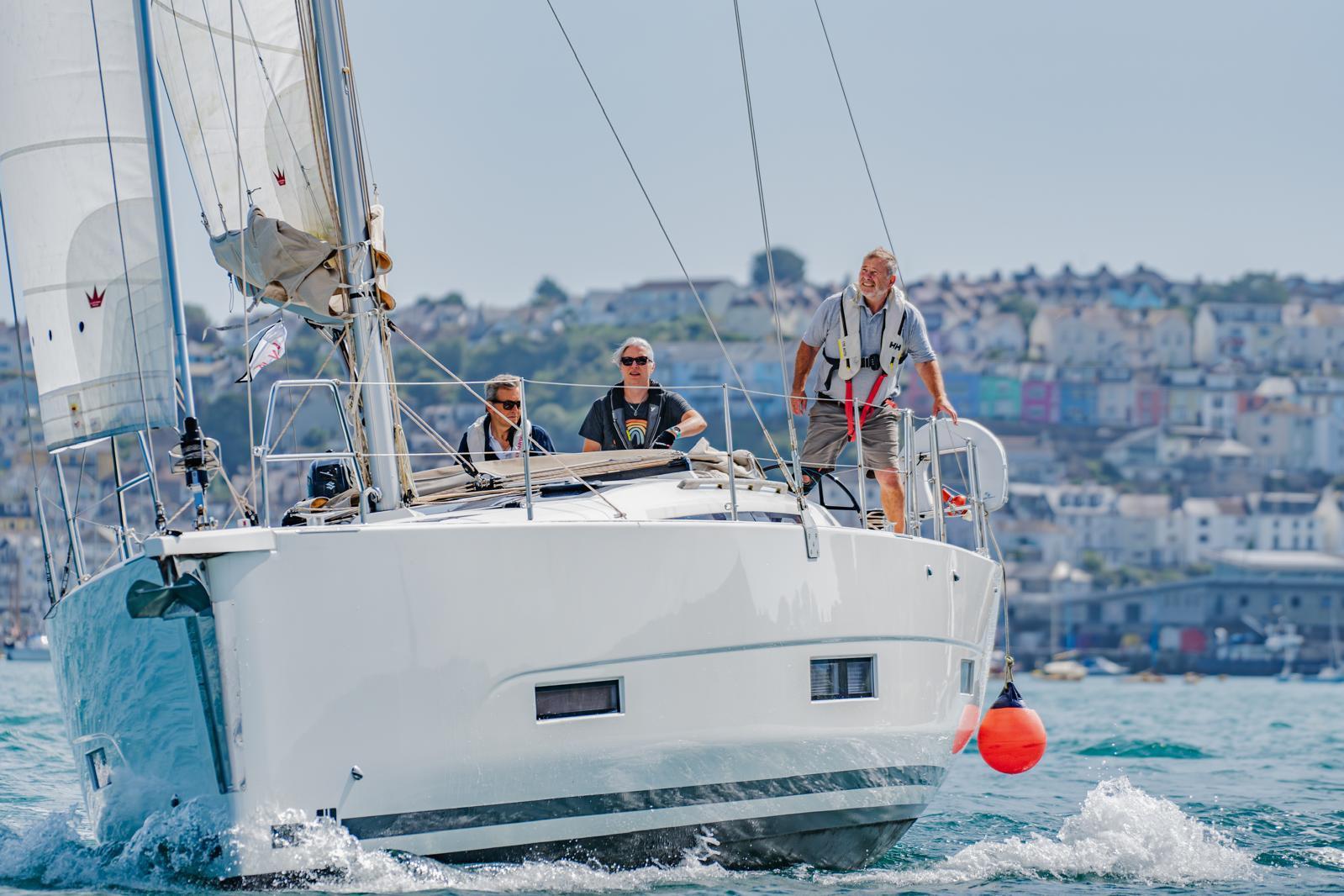 Sailing on a 2021 Dufour 390 yacht with crew, coastal town in background.