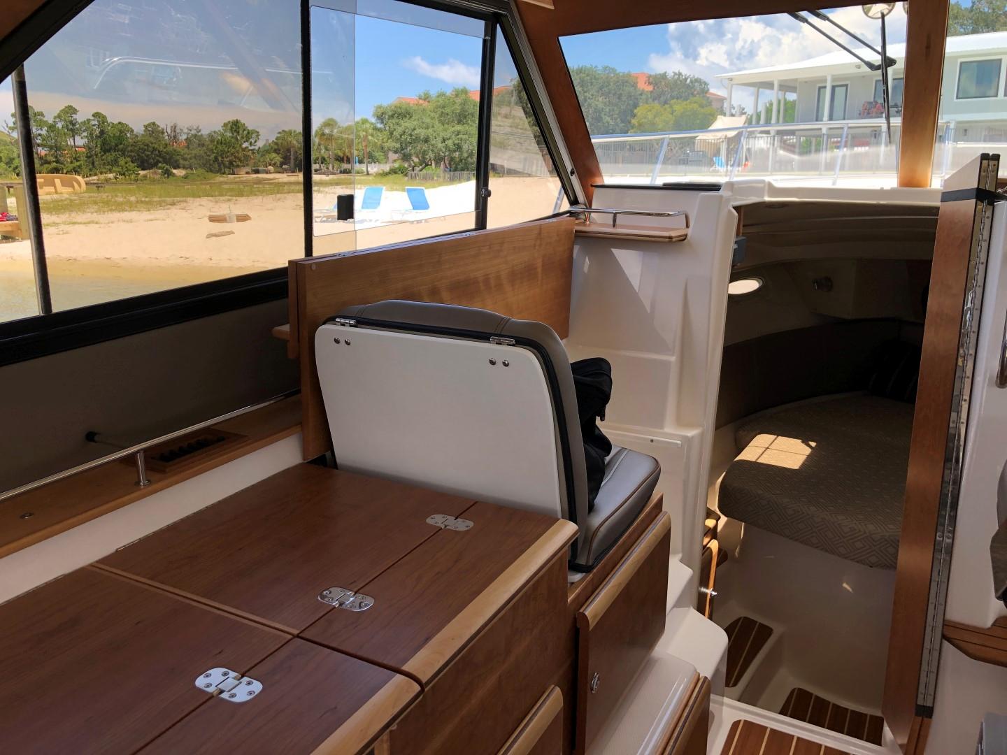 Cutwater-C-32 CB 2025-C32 CB 2025 FL-US-2025 Cutwater C-32 CB boat interior with wood finish and seating, docked near a sandy beach.-9832181 | Thumbnail