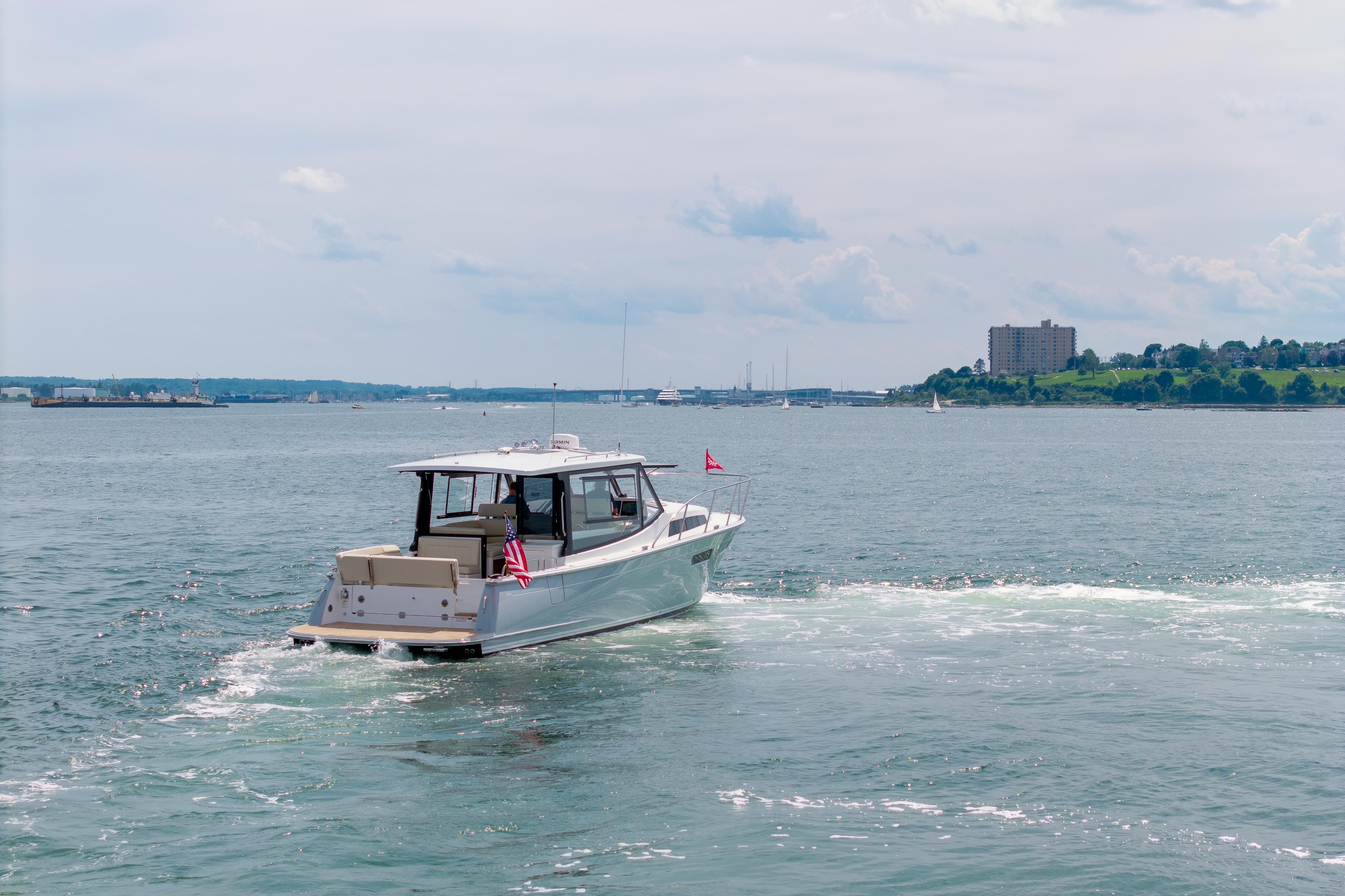 2025 MJM 42 boat cruising on a scenic waterfront with distant cityscape.