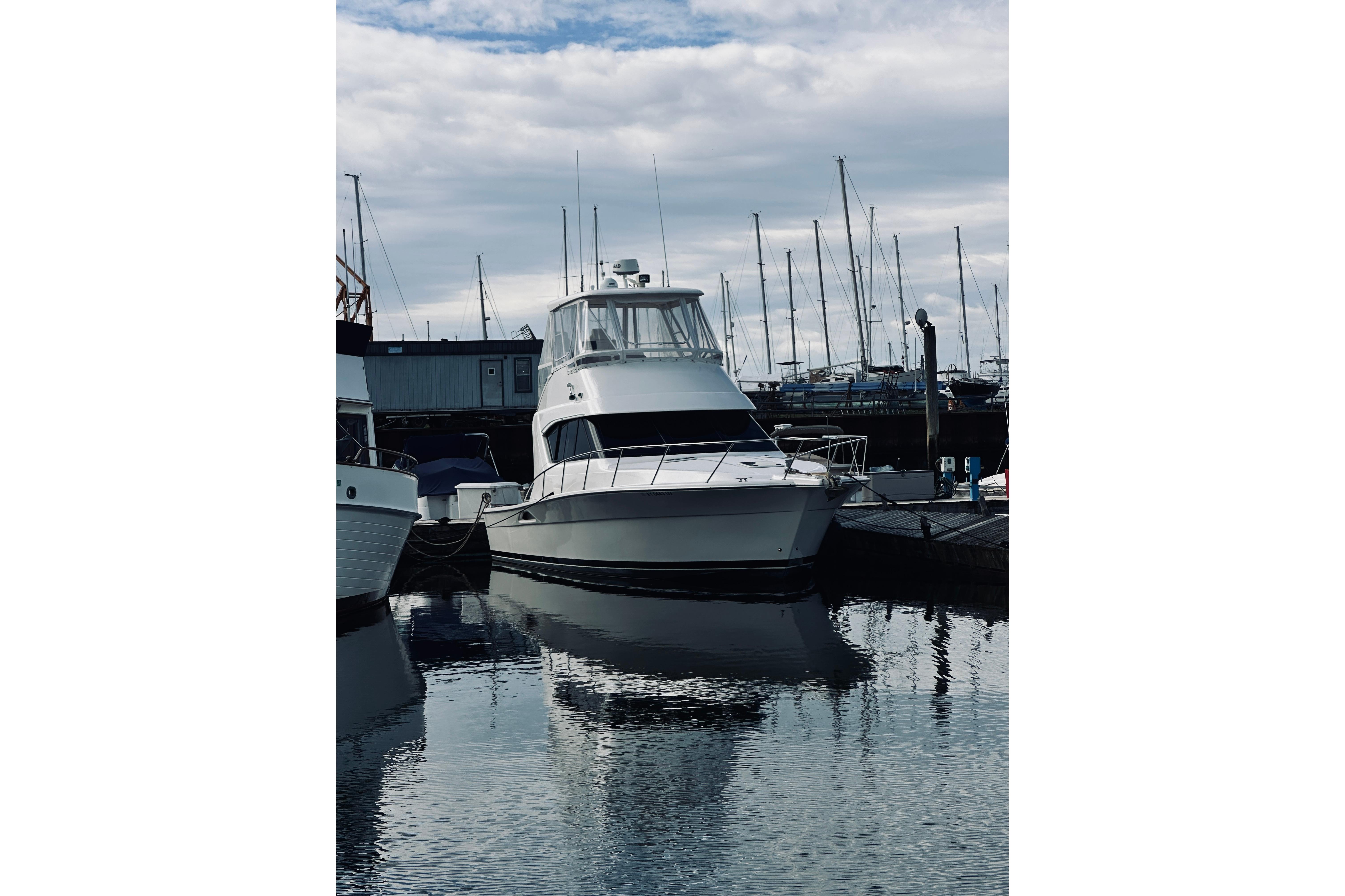 2000 Riviera 40 yacht docked at marina, reflecting on calm water under cloudy sky.