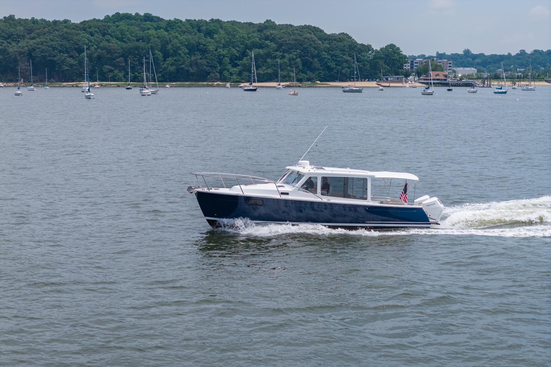 2025 MJM 35 boat cruising on a scenic lake with sailboats and lush green shoreline.