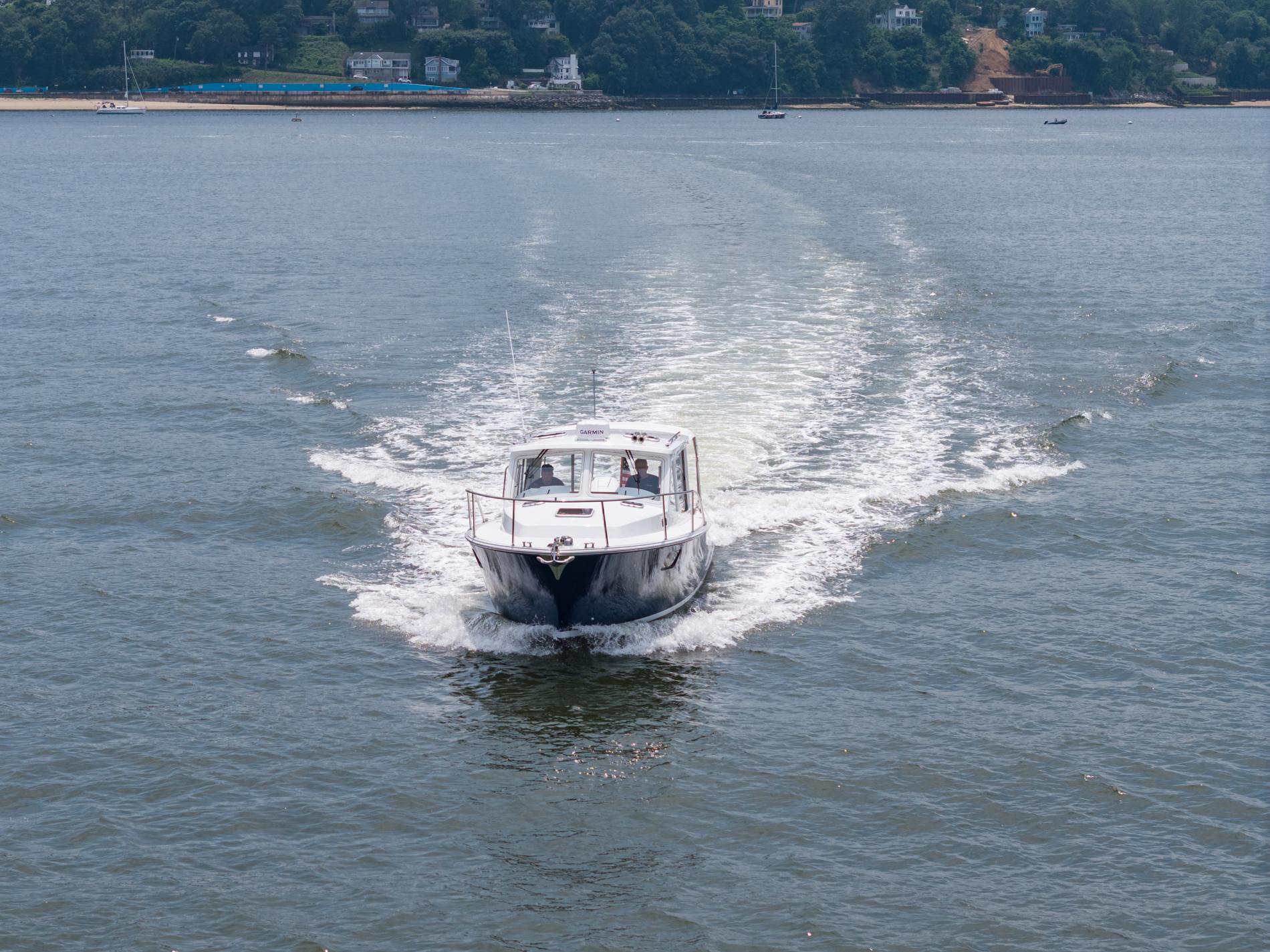 MJM 35 boat cruising on water, 2025 model, with scenic shoreline background.