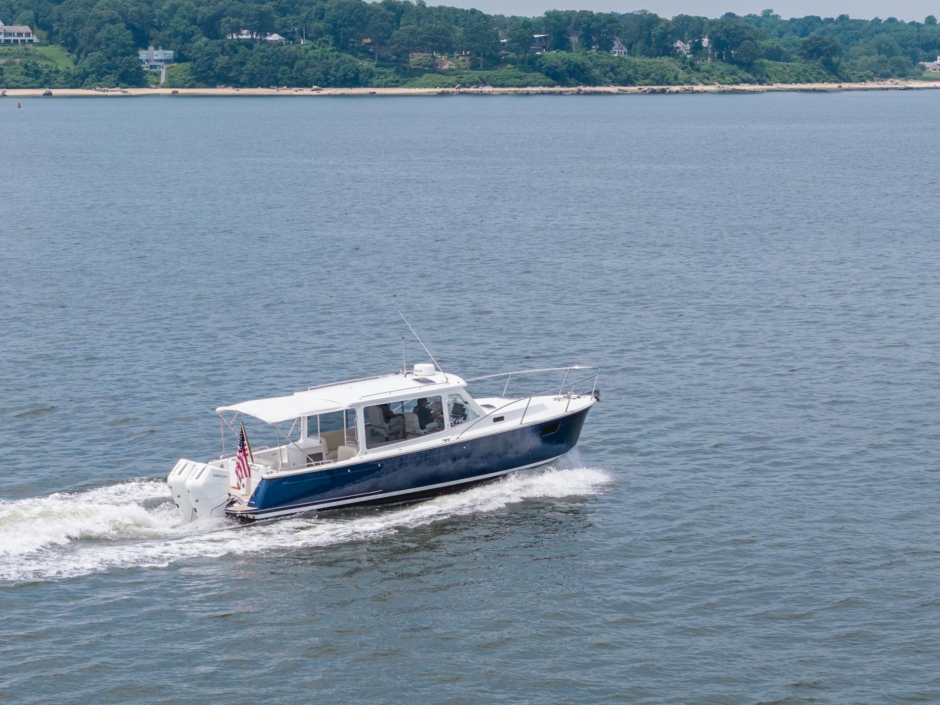 2025 MJM 35 boat cruising on a calm lake with lush green shoreline.