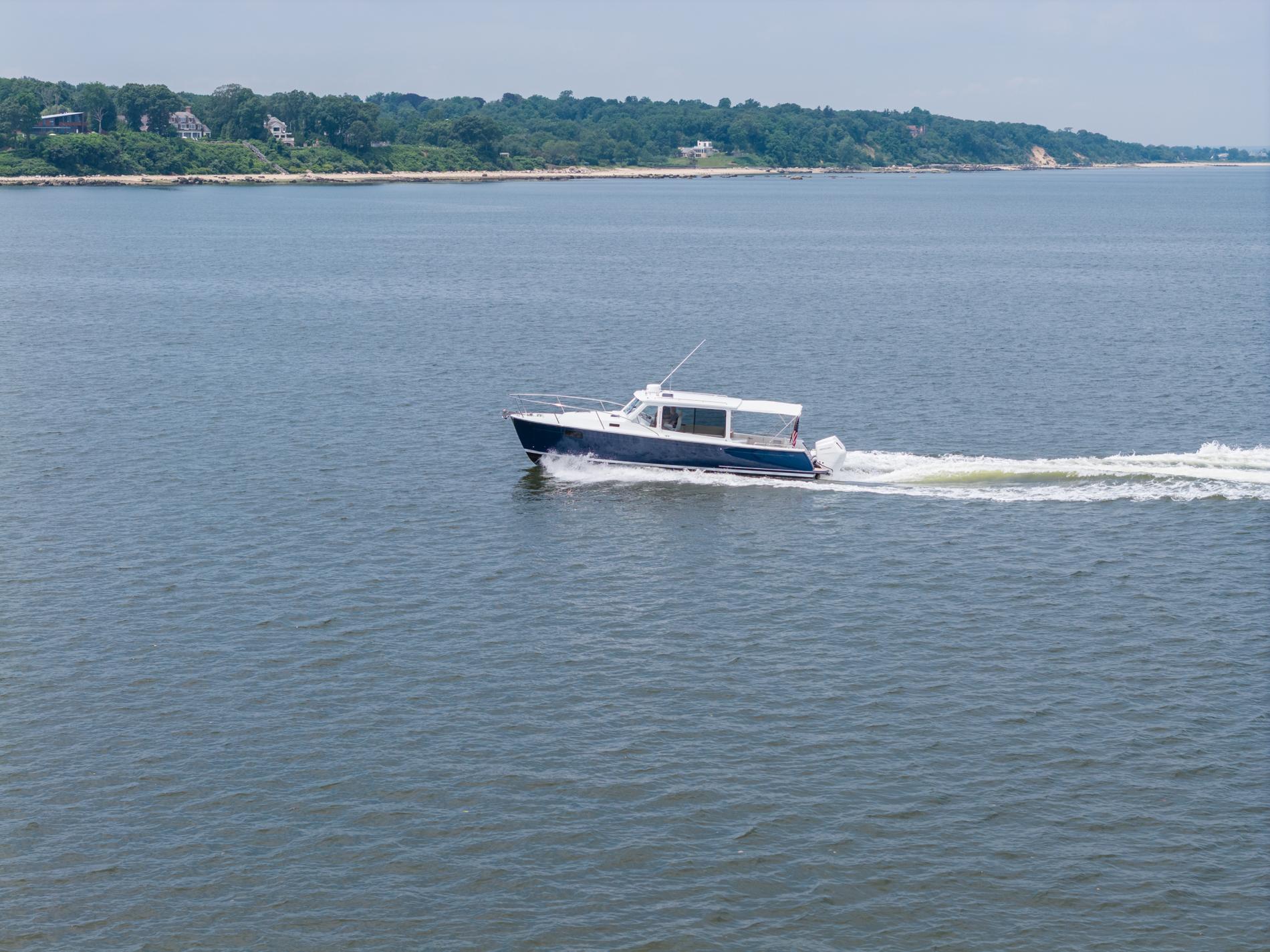 2025 MJM 35 boat cruising on open water near a lush coastline.