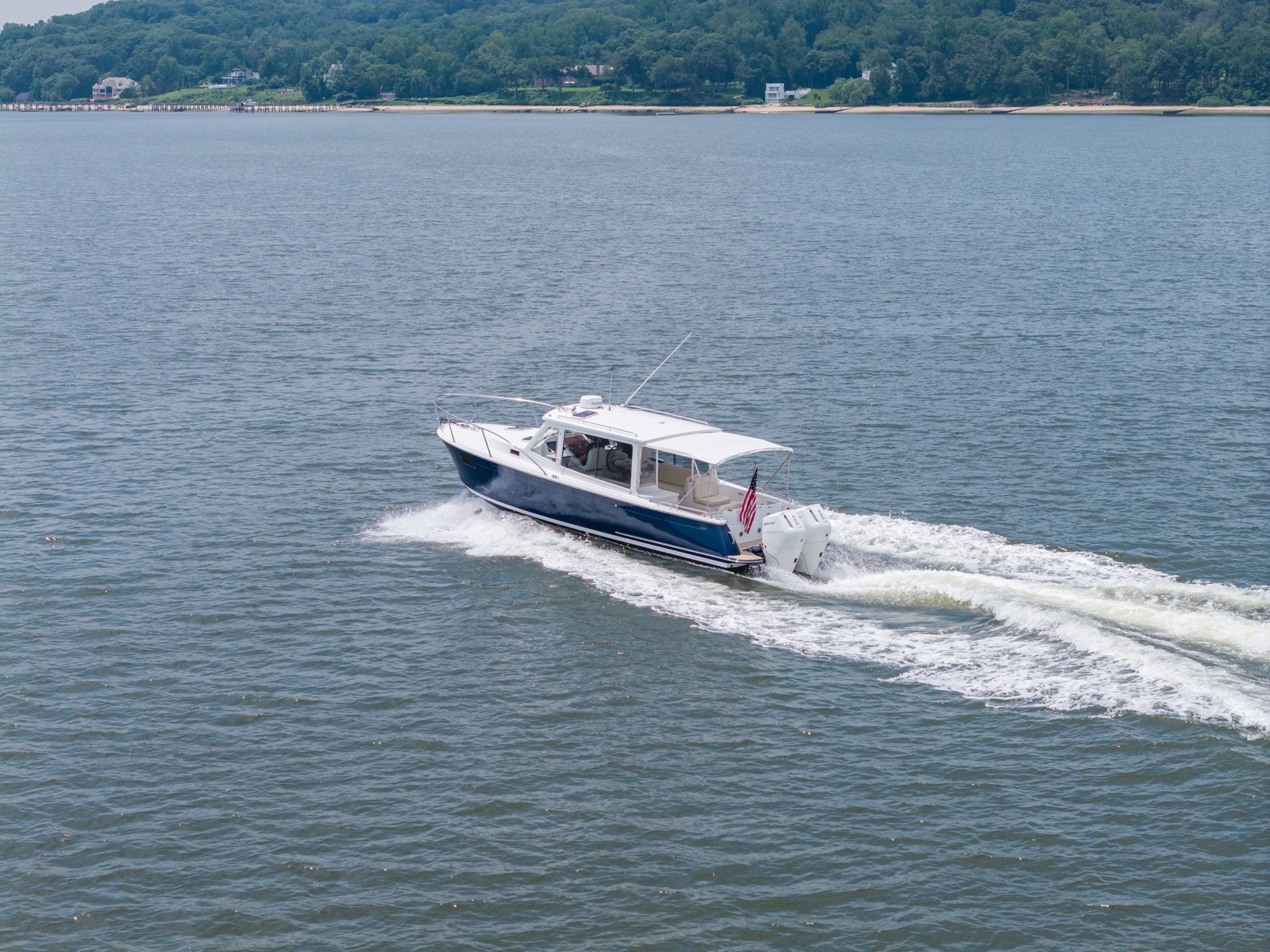 2025 MJM 35 boat cruising on a calm lake with forested shoreline.