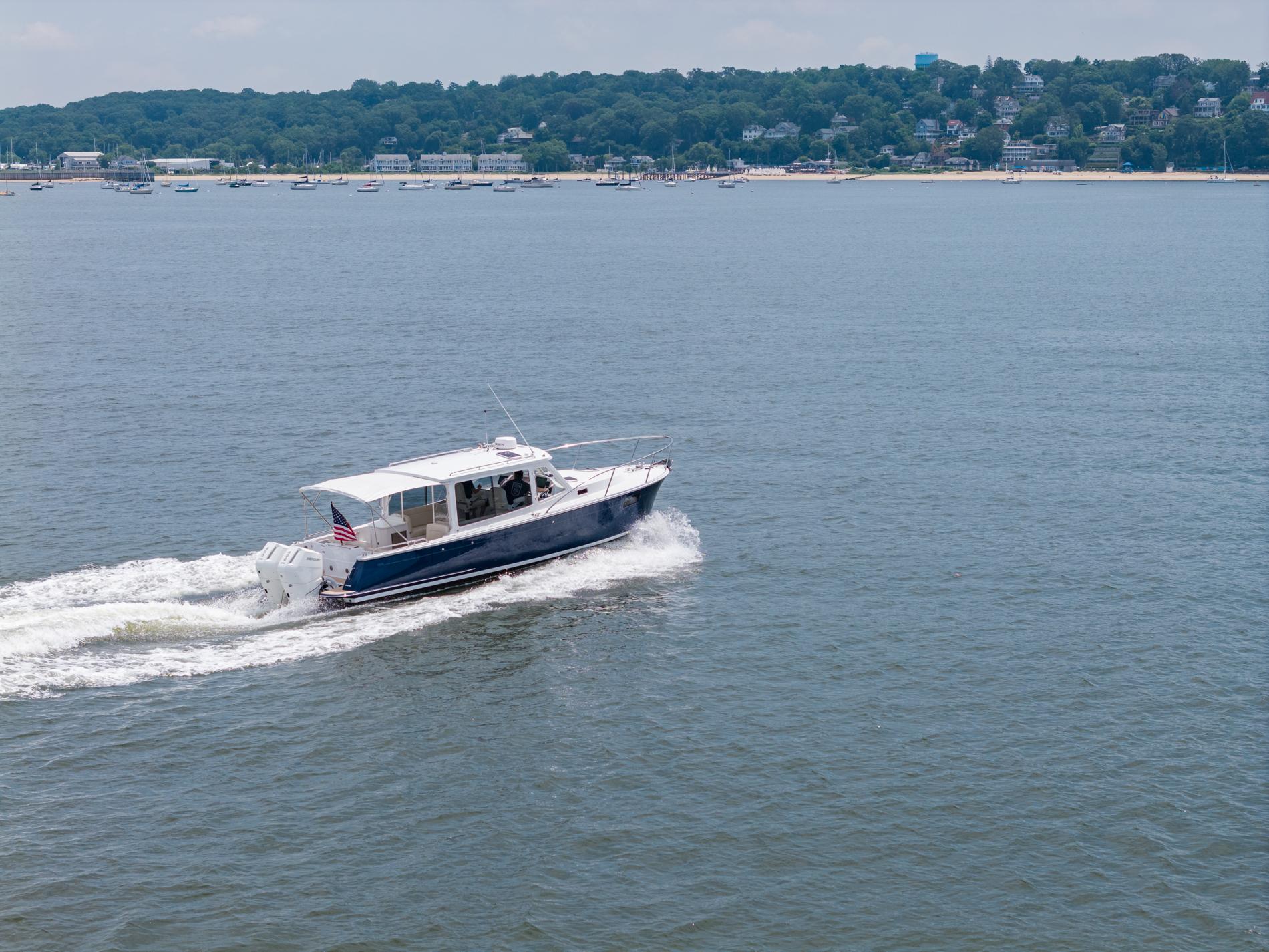2025 MJM 35 boat cruising on a calm lake with a scenic shoreline backdrop.