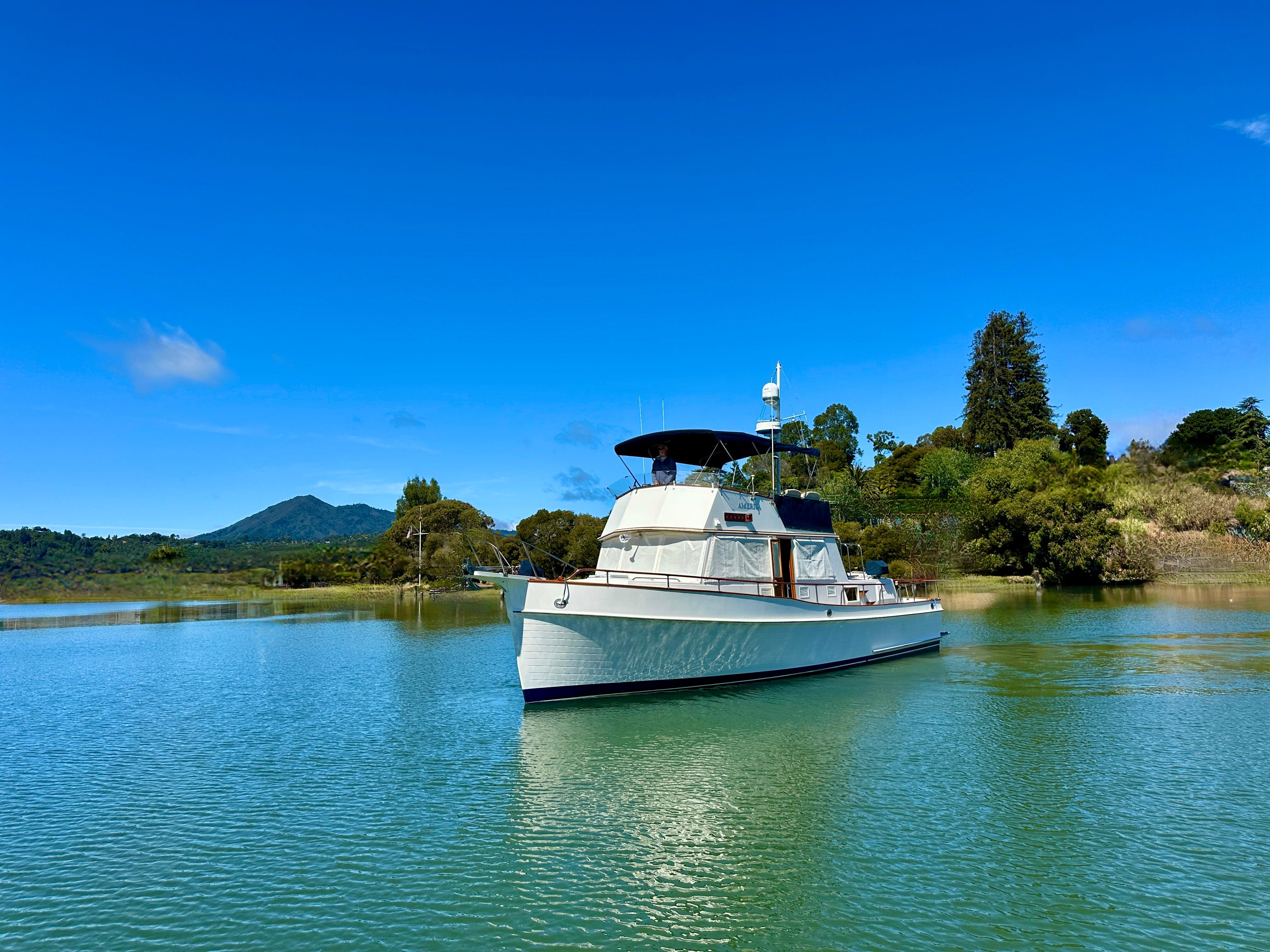 1989 Grand Banks 42 Classic yacht on tranquil water with lush greenery and blue sky.
