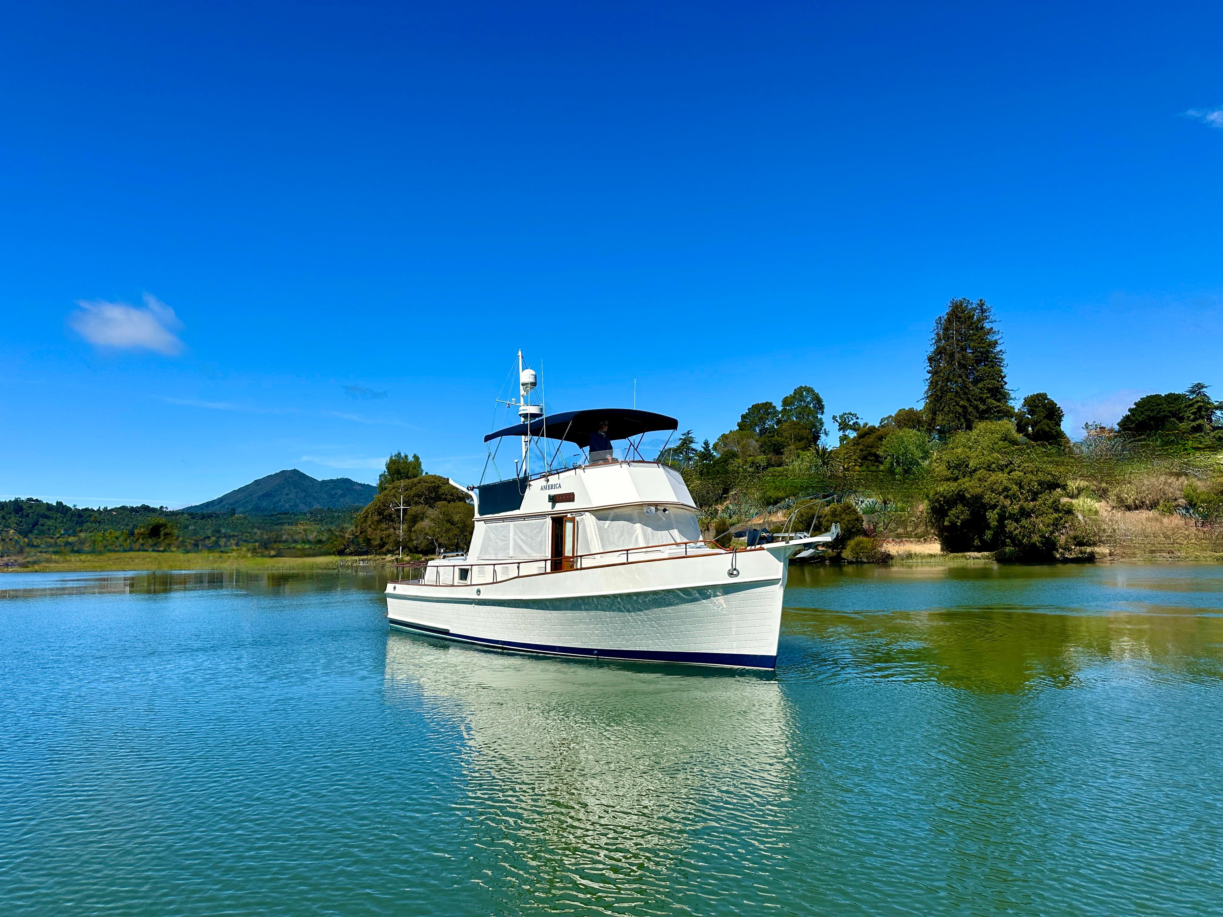 1989 Grand Banks 42 Classic yacht on serene water with lush green landscape.