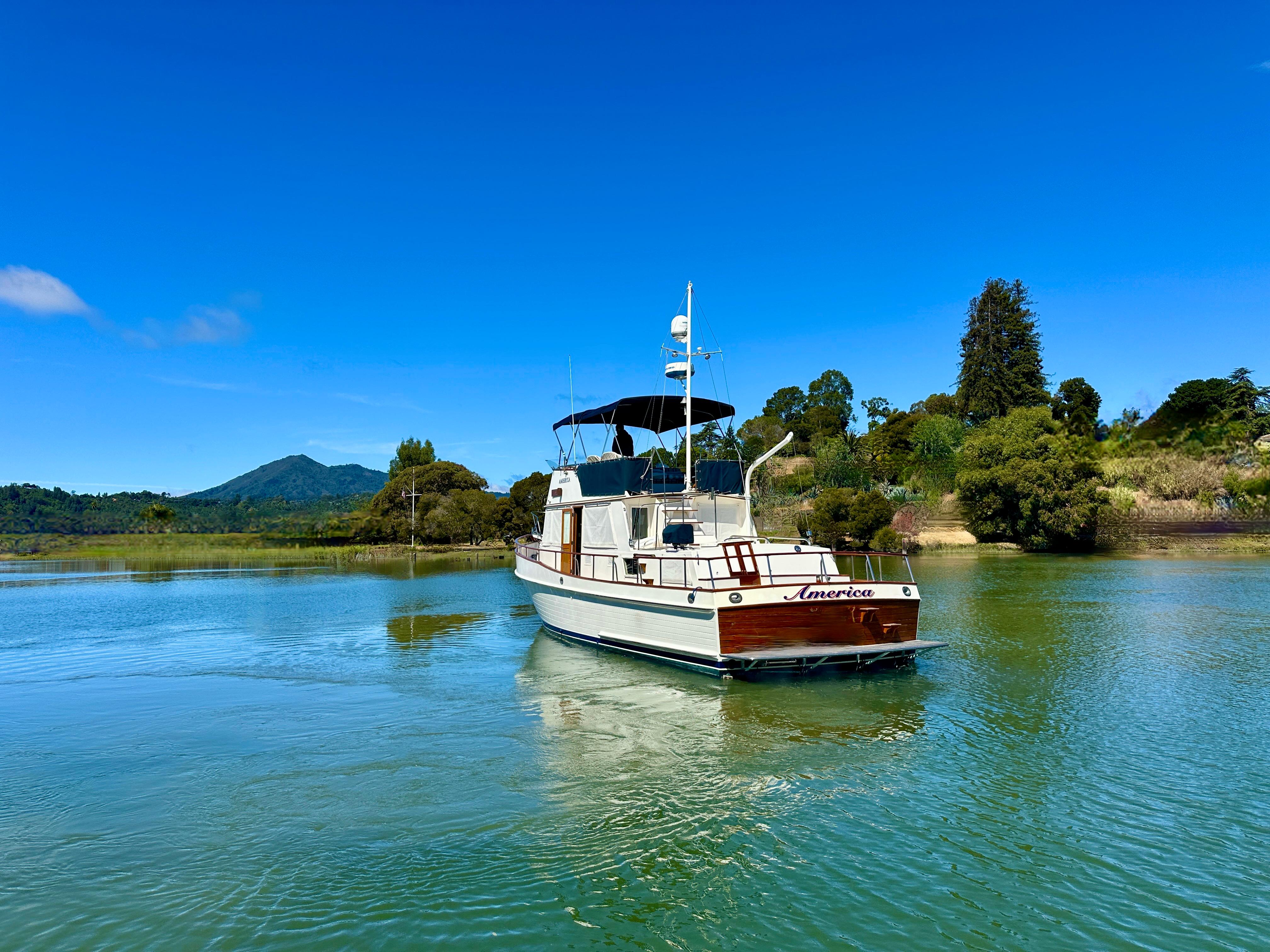 1989 Grand Banks 42 Classic yacht on serene water with lush greenery backdrop.