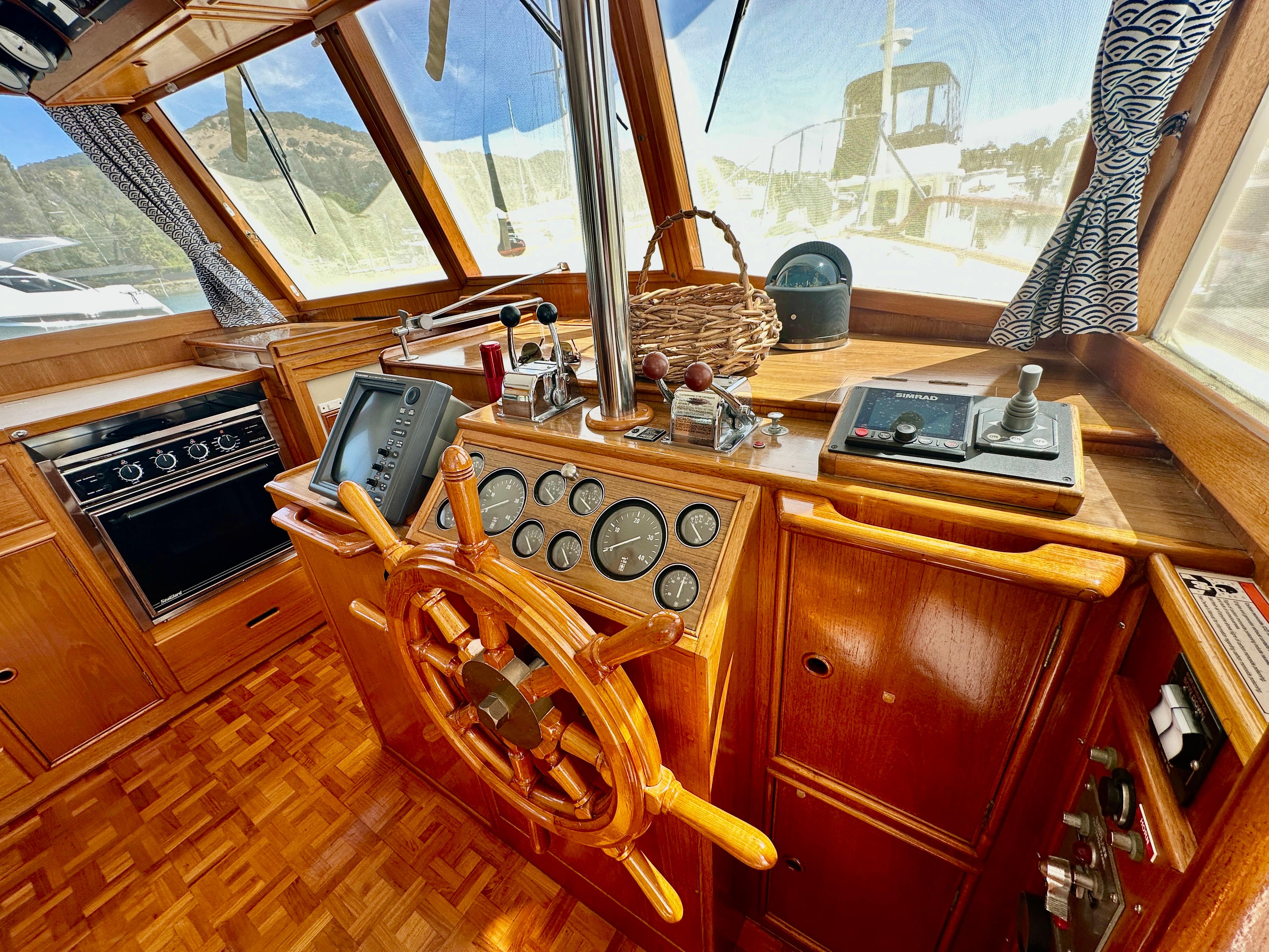 1989 Grand Banks 42 Classic helm with wooden wheel, navigation instruments, and panoramic windows.