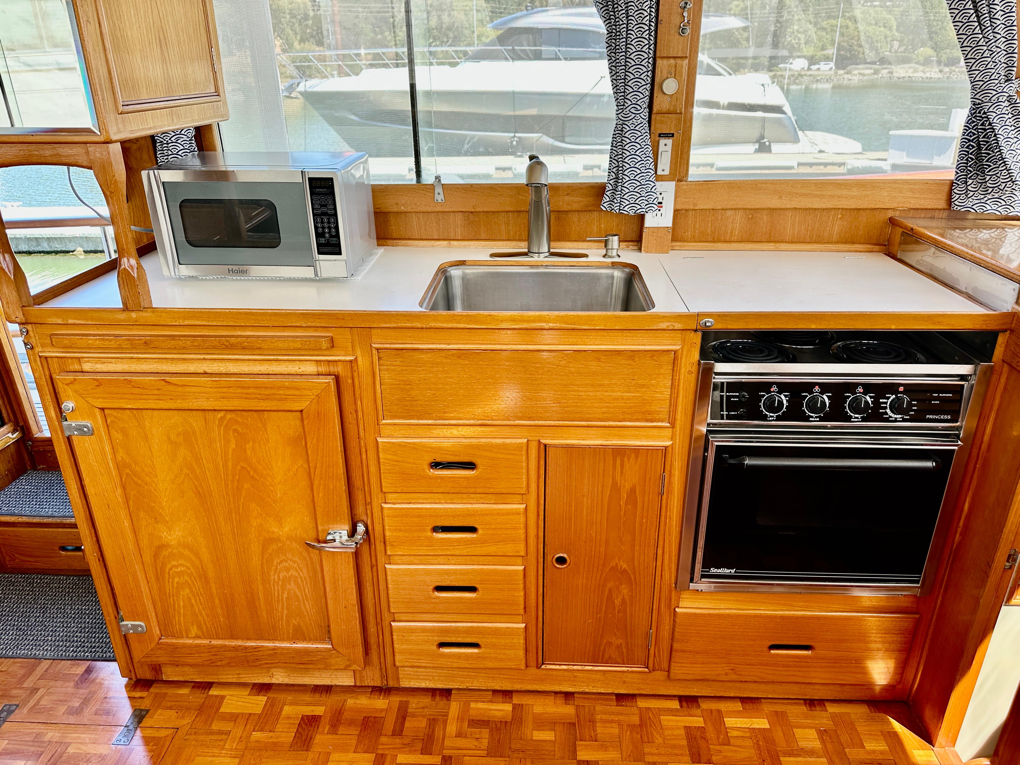 Wooden kitchen interior of 1989 Grand Banks 42 Classic yacht with stove, sink, and microwave.
