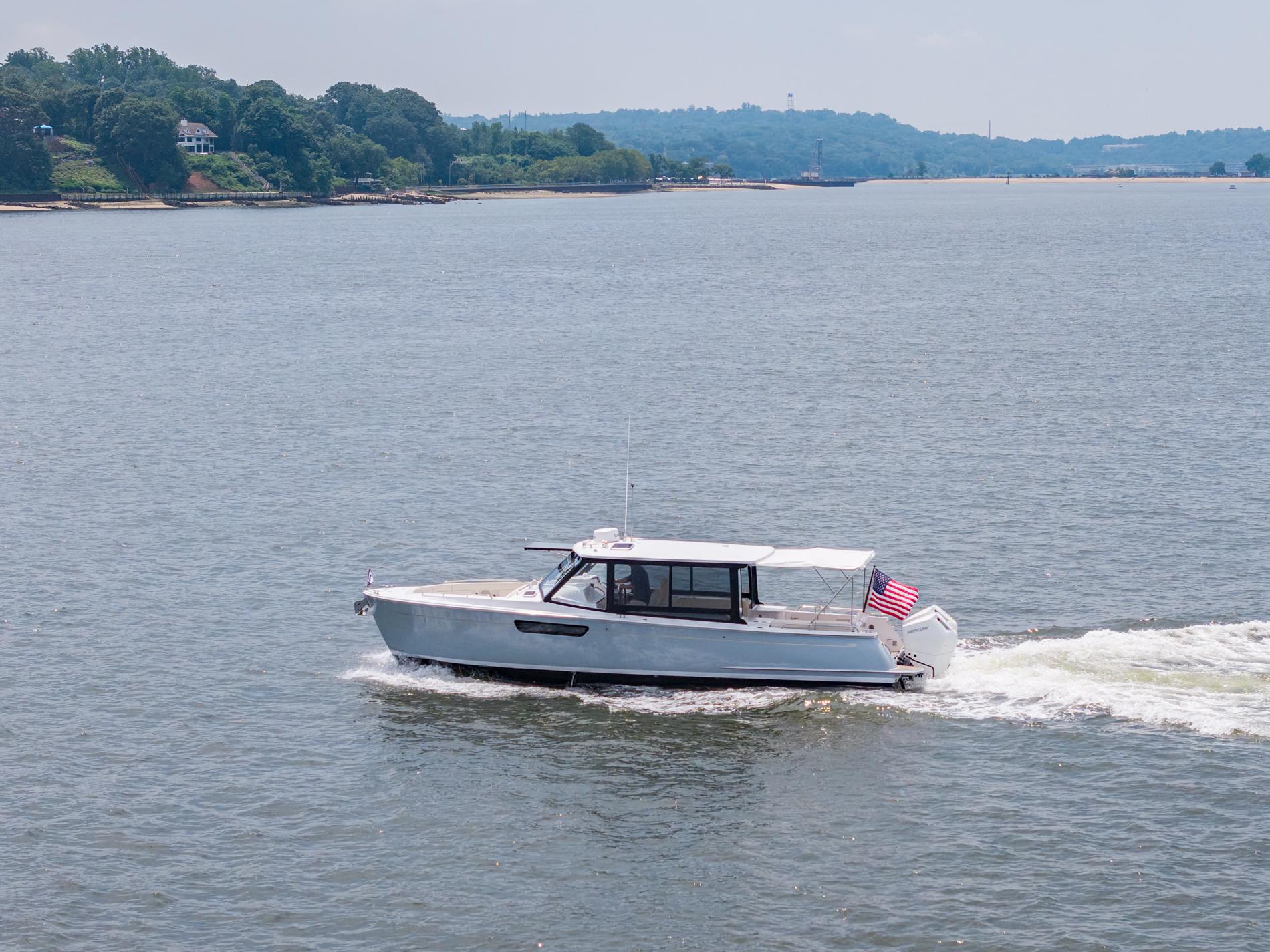 2025 MJM 3 boat cruising on a scenic lake with lush green shoreline.