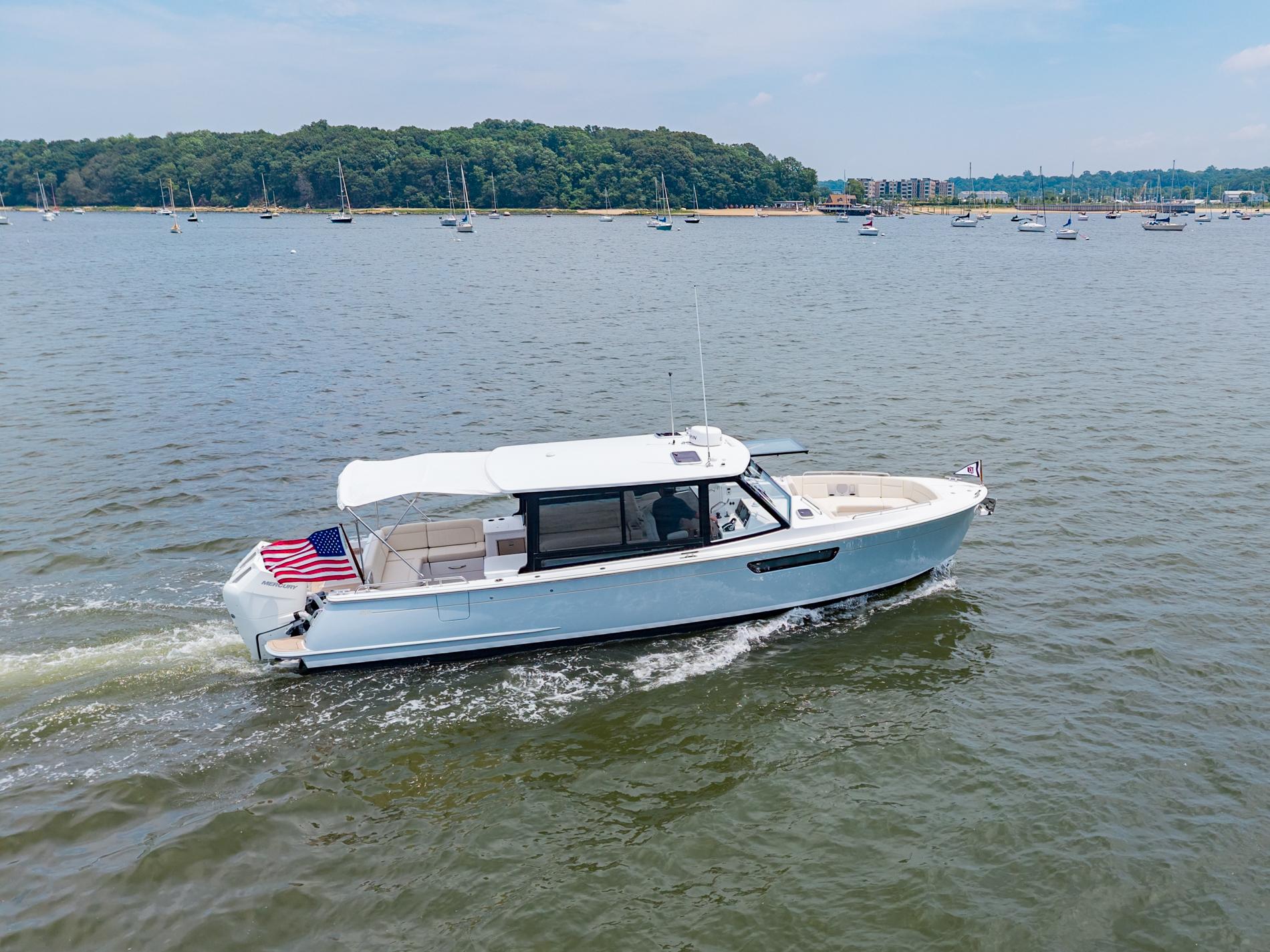 2025 MJM 3 boat cruising on a scenic lake with lush green shoreline.